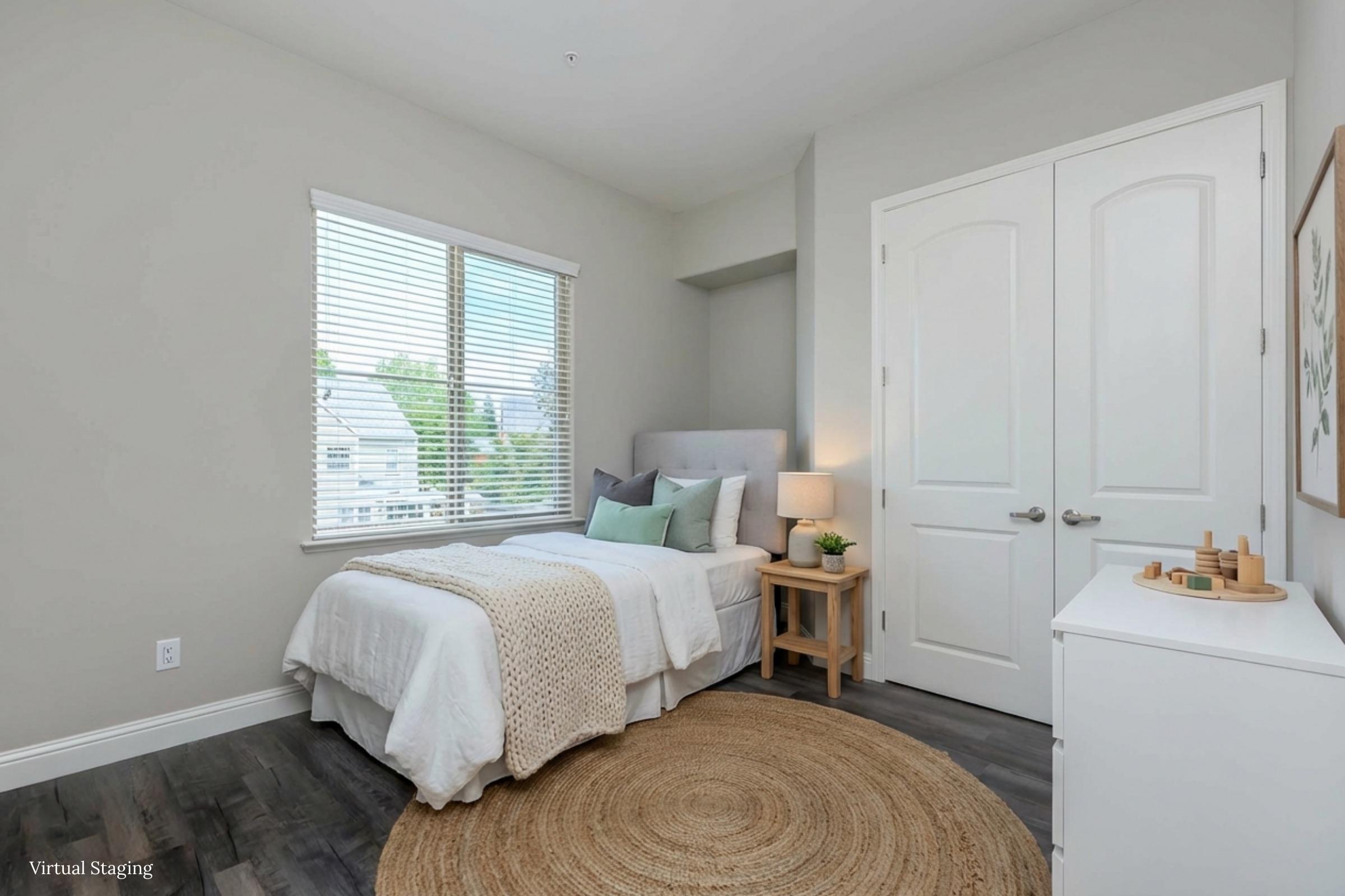 A cozy, well-lit bedroom featuring a single bed with a light-colored blanket, a small nightstand with a lamp, and a decorative rug on the floor. There are light green accents in the decor, a large window allowing natural light, and minimalistic furniture creating a simple and inviting atmosphere.