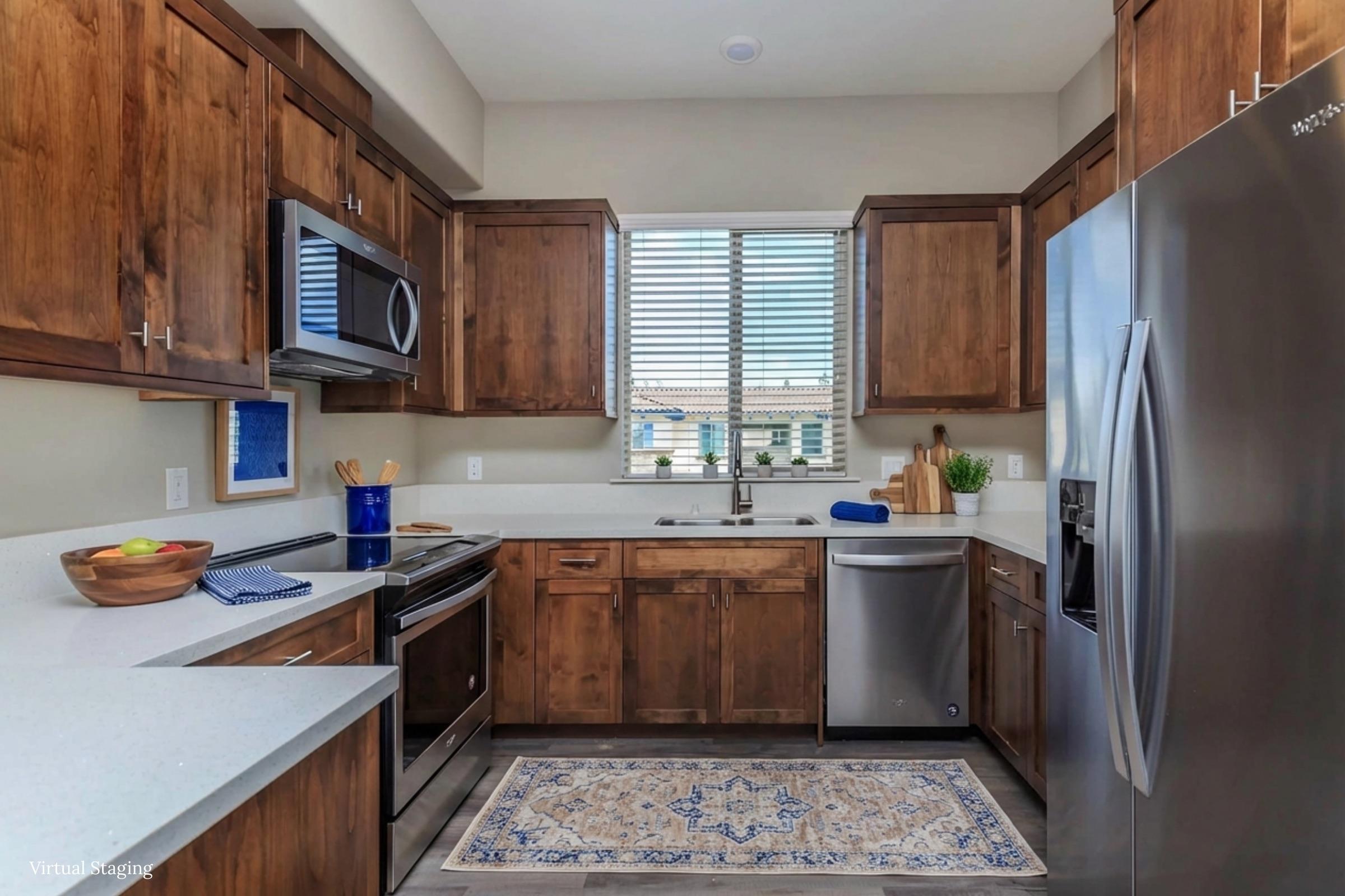 Modern kitchen featuring wooden cabinets, stainless steel appliances, and a white countertop. A window with blinds allows natural light, and there’s a blue backsplash behind the sink. A fruit bowl is on the counter, and a decorative rug adds a cozy touch to the space.