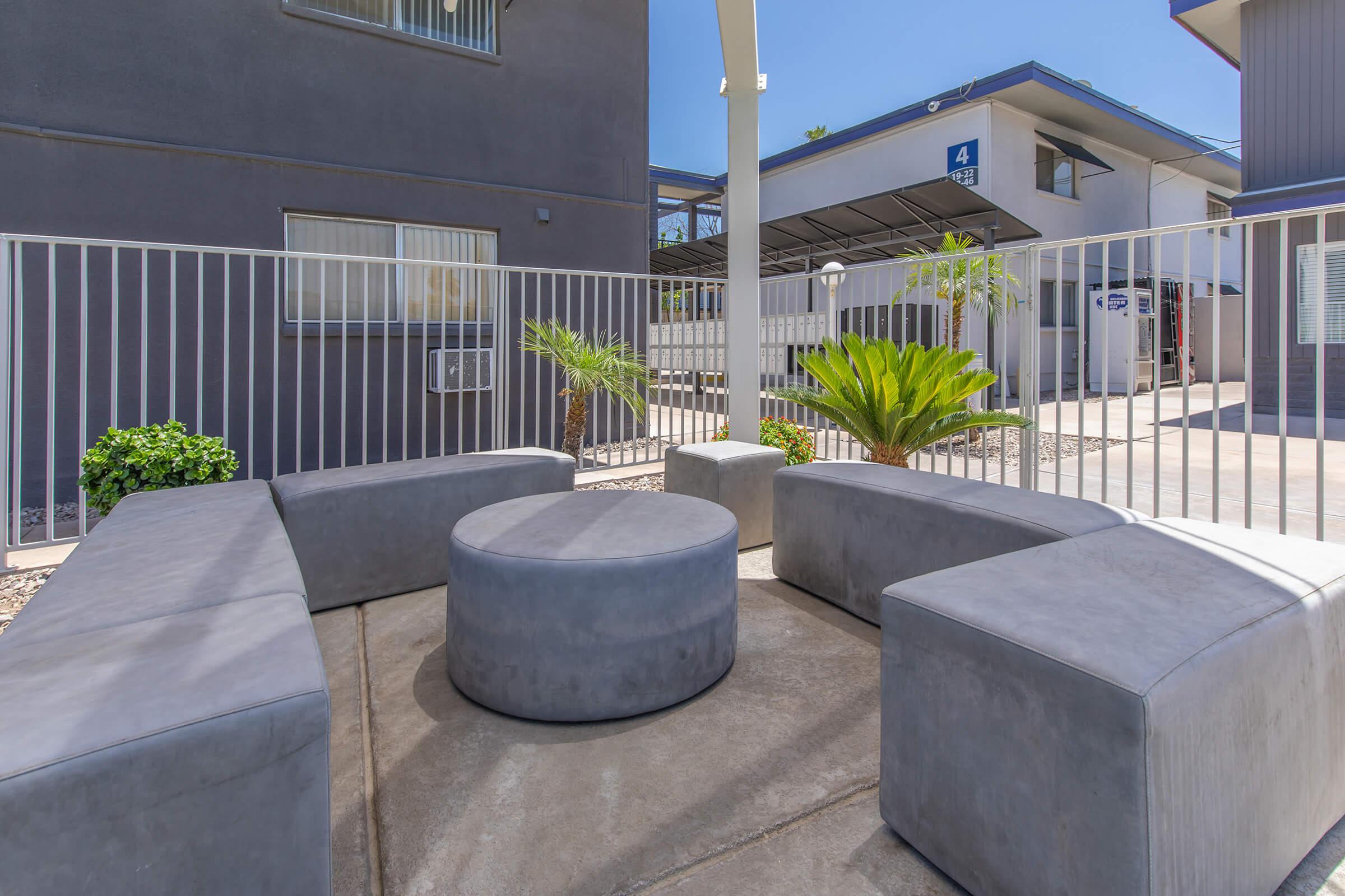 Outdoor sitting area surrounded by plants and a large white fence with Phoenix apartments in the back