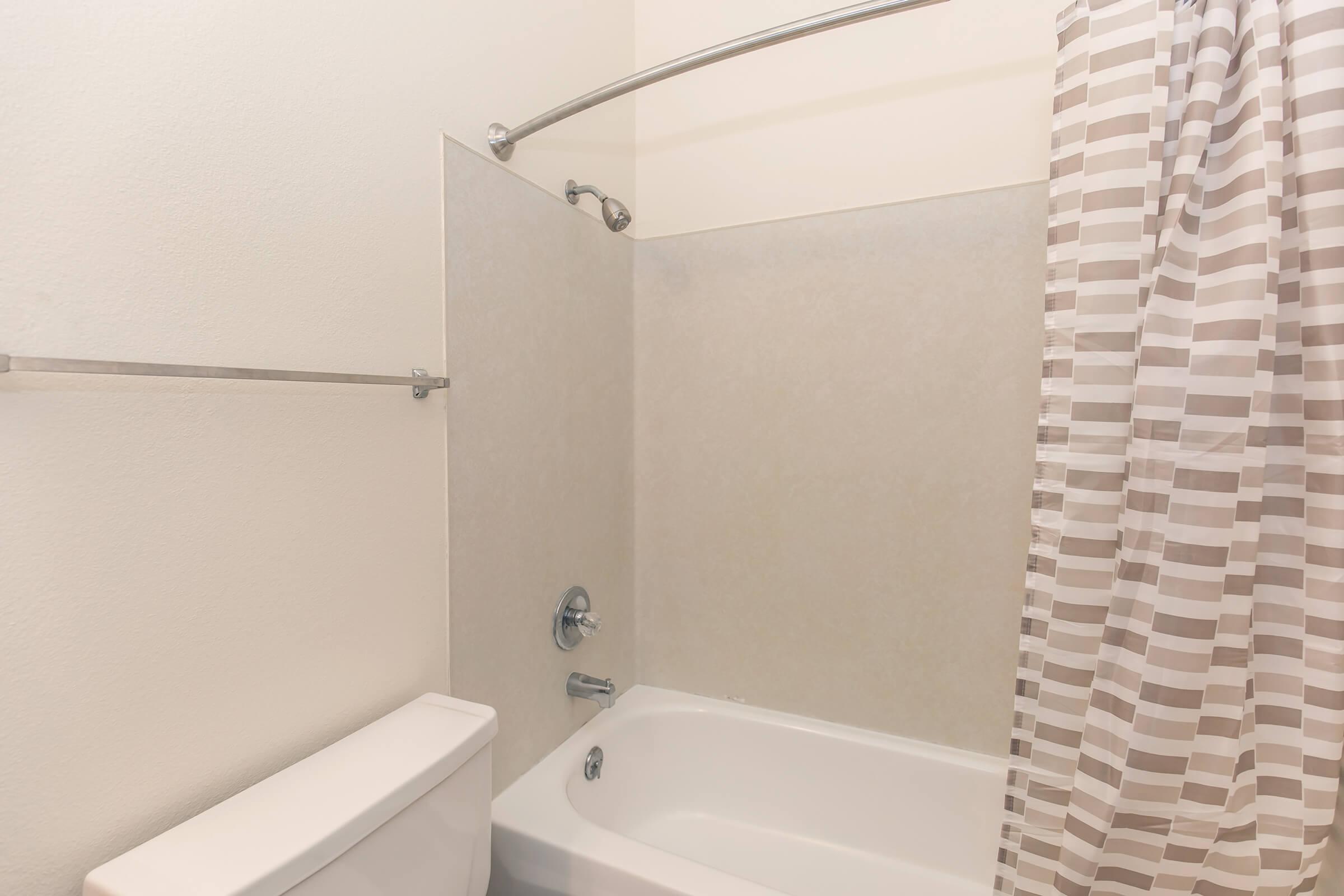 A bathroom featuring a bathtub with a shower curtain and a toilet. The walls are painted a light color, and the shower curtain has a striped pattern. A curved shower rod is installed above the bathtub. The overall space appears clean and minimalistic.