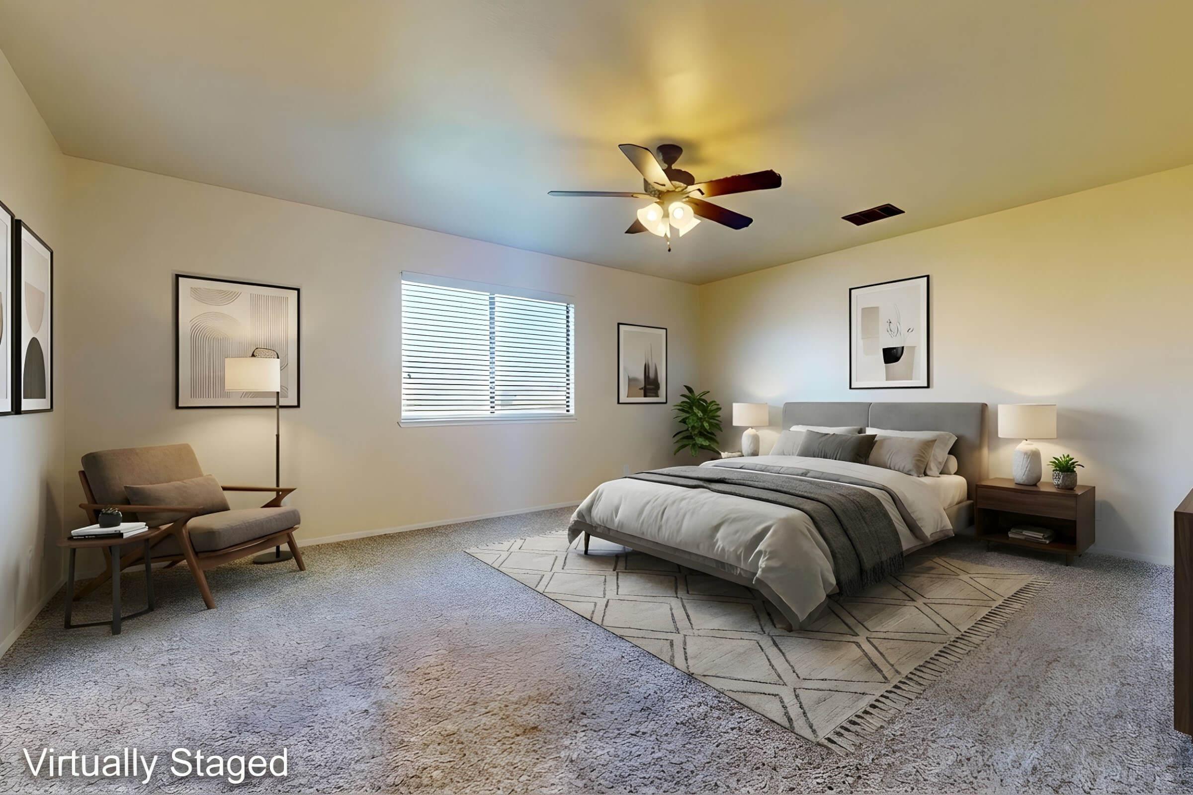 A virtual staging of a bedroom featuring a large bed with gray bedding, a decorative throw, and two framed pictures on the walls. A light-colored armchair and a bedside table with a lamp are visible. A ceiling fan and natural light from a window enhance the cozy atmosphere.