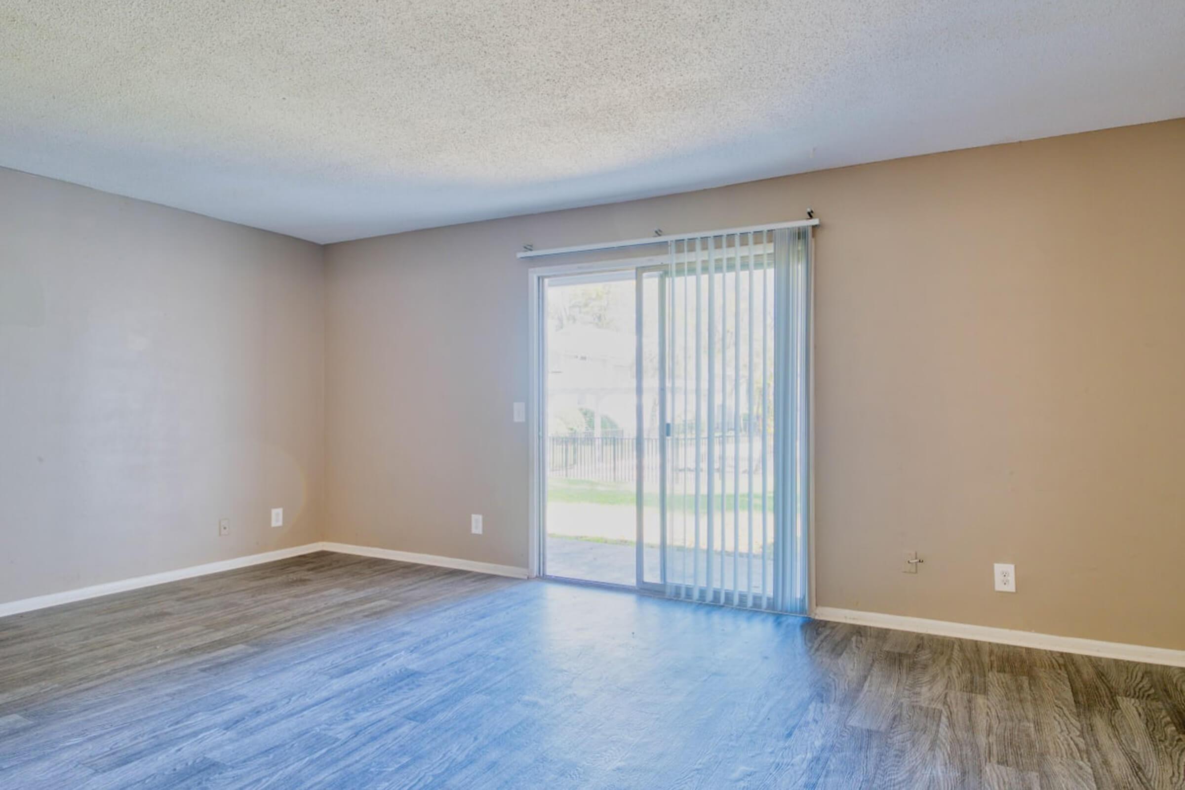 Empty room with light brown walls and a sliding glass door leading to an outdoor area. The floor is covered in light-colored laminate, and the space is brightly lit. There are no furnishings, creating a spacious and open atmosphere.