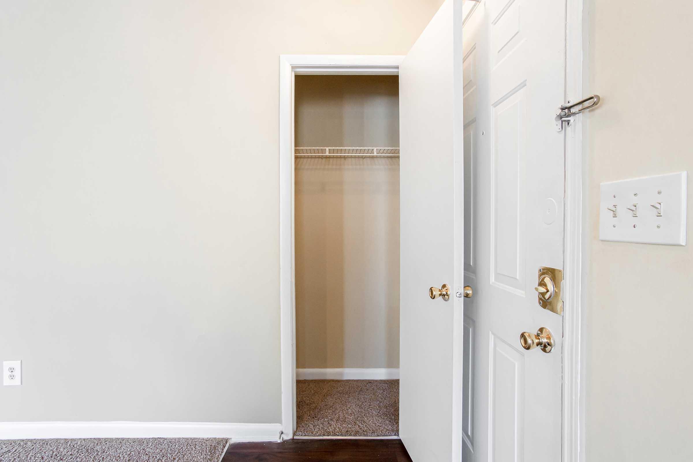 Interior view of a room showcasing an open door leading to a closet space. The walls are painted a light color, and the floor is covered with carpet. The closet features a simple shelving unit, and there is a door handle visible on both the room and closet doors.
