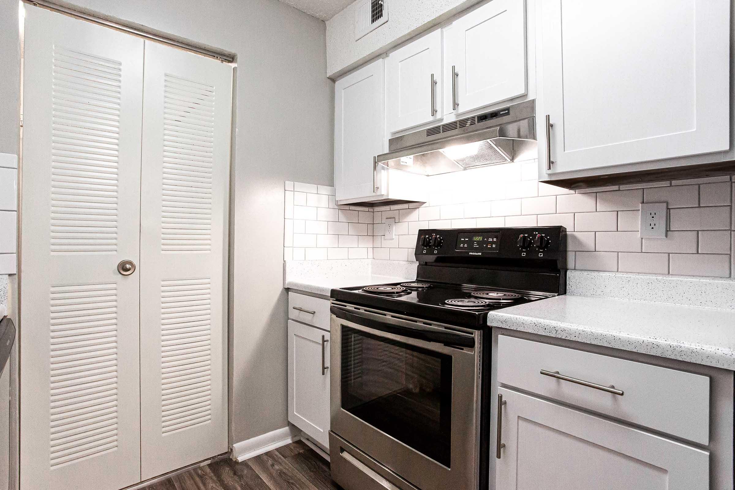 Modern kitchen featuring a clean design with white cabinets, a stainless steel stove, and sleek countertops. The backsplash is made of white tiles, and there's a sliding door providing access to storage. The overall ambiance is bright and airy, complemented by soft lighting.