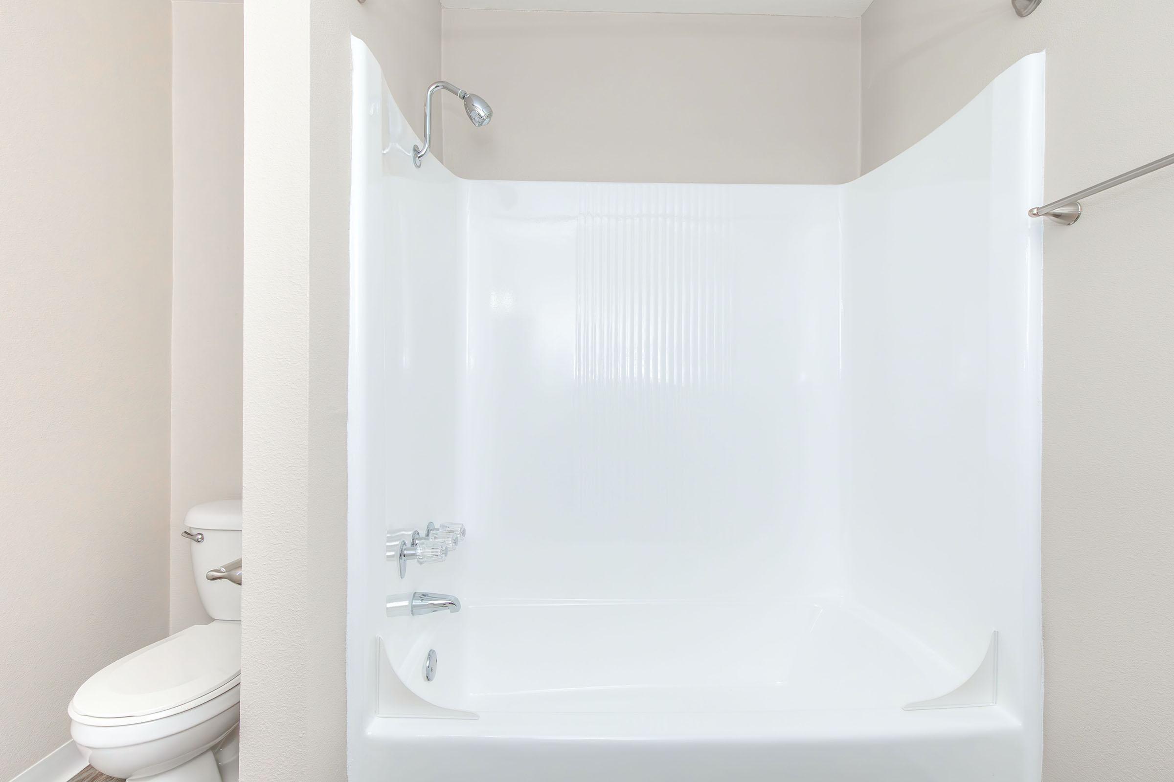 A clean, modern bathroom featuring a white shower stall with a built-in bathtub, a showerhead above, and a simple bathroom design. A white toilet is visible in the background, with neutral-colored walls creating a bright and airy atmosphere.