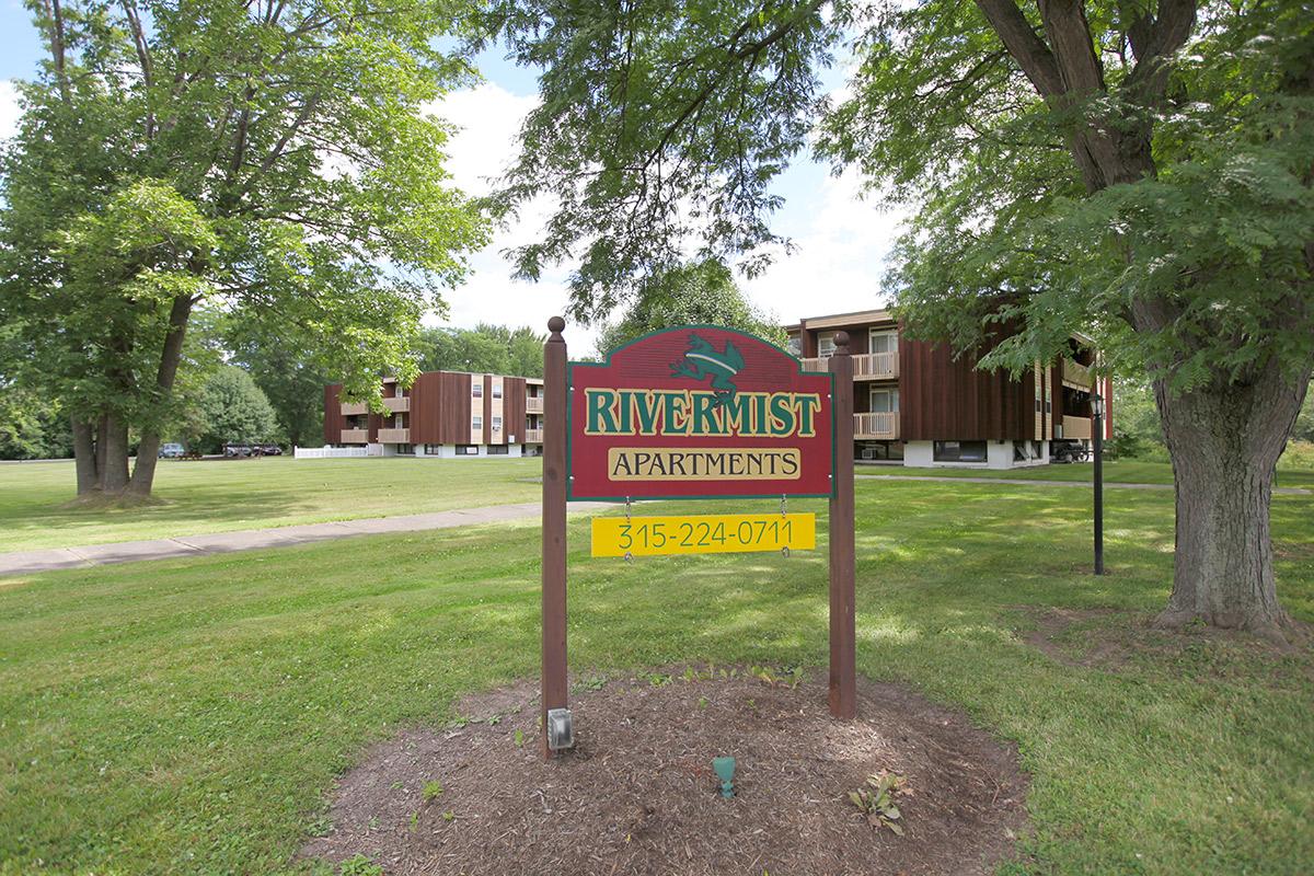 a sign over a grassy area with trees in the background