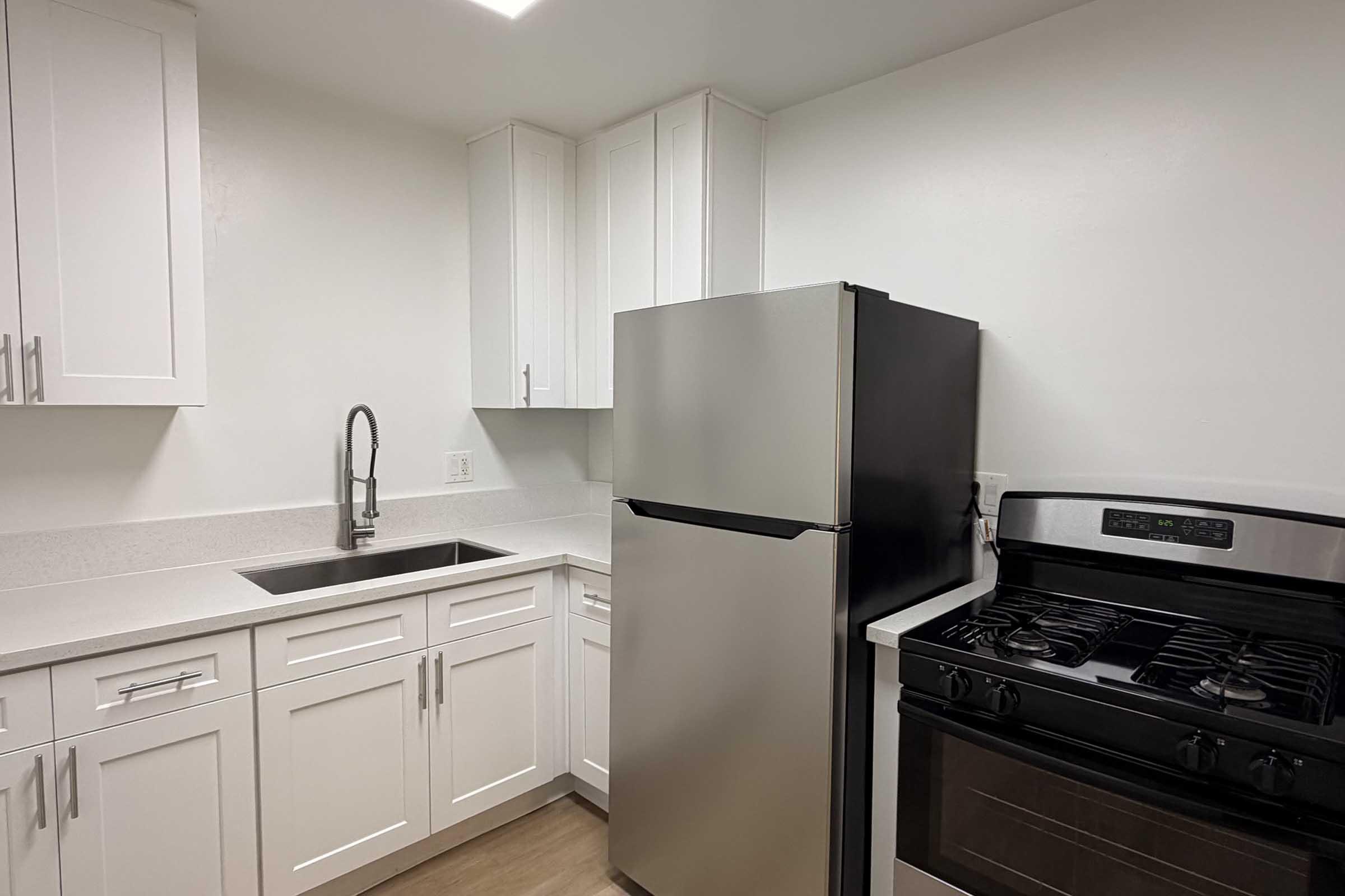 Modern kitchen featuring white cabinetry, a silver refrigerator, a stainless steel sink with a sleek faucet, and a gas stove. The countertops are light-colored, creating a bright and clean aesthetic in a compact layout.