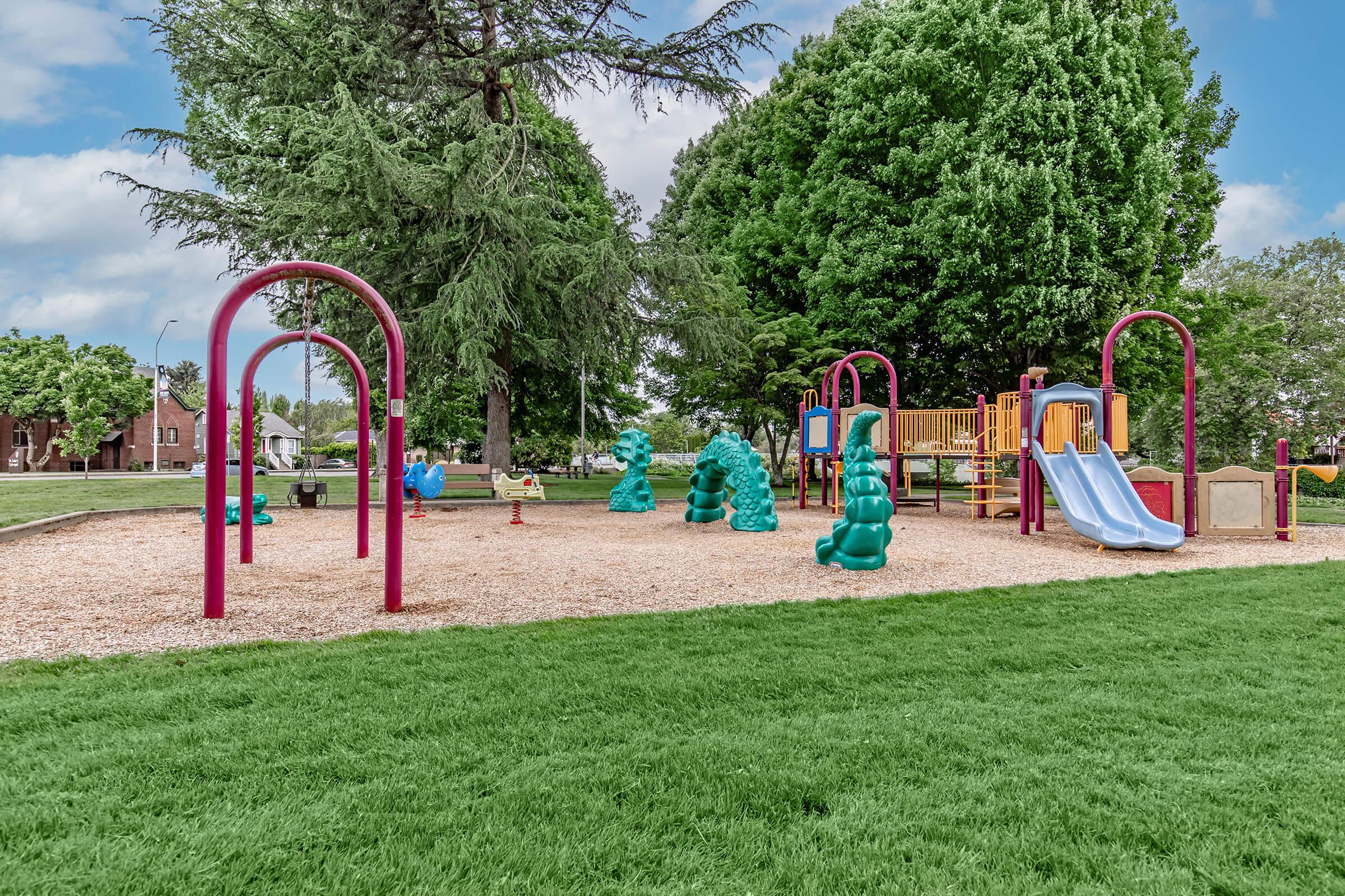 Colorful playground equipment including slides, climbing structures, and play areas, surrounded by green grass and trees. The scene is bright and inviting, perfect for children to play and explore.