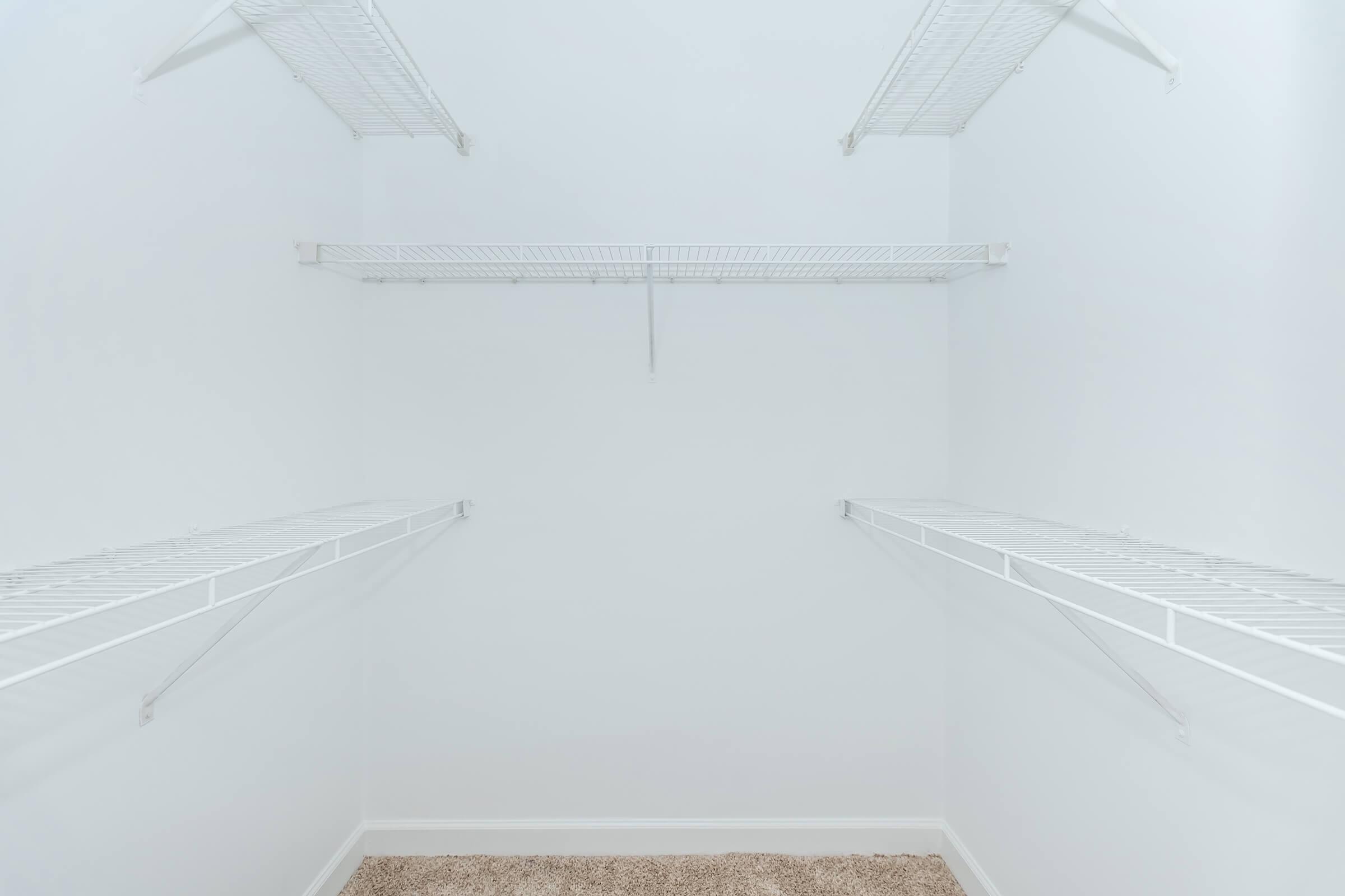 Empty closet with white wire shelving along the walls, no items or decorations present, featuring light-colored walls and a soft carpeted floor.