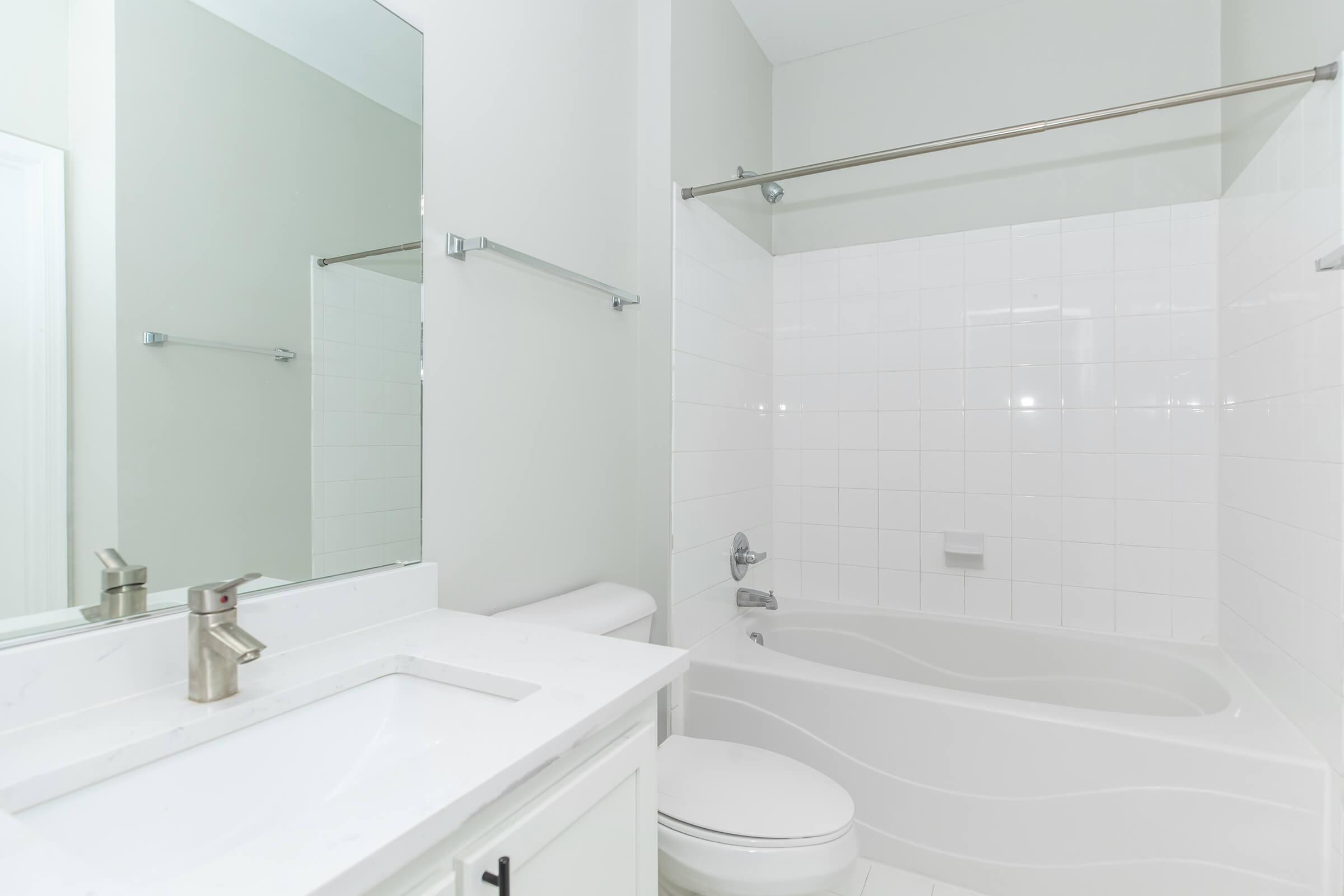 Modern bathroom featuring a white tiled shower and tub combination, a sleek sink with a faucet, a mirror above the sink, and a minimalistic design. The walls are painted in a light color, and there are chrome fixtures for a clean and polished look.