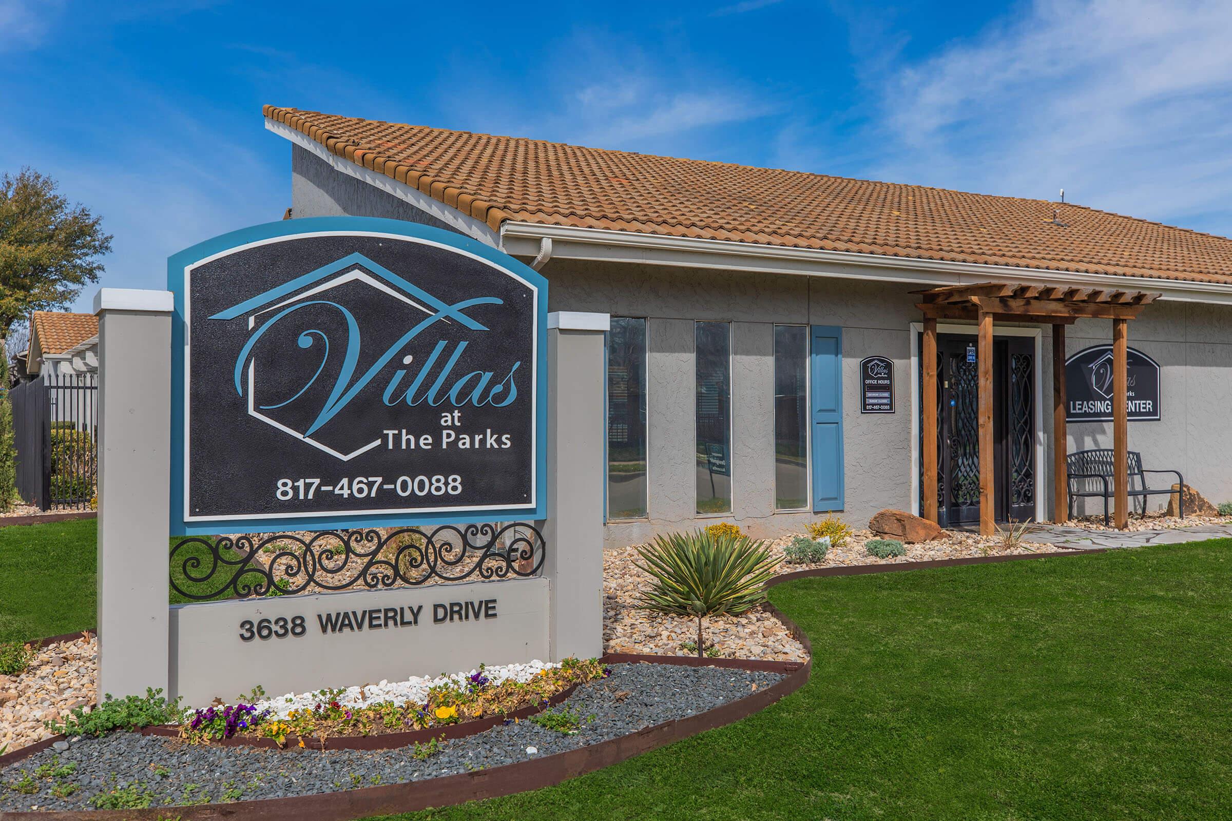 Sign for "Villas at The Parks," displaying contact number 817-467-0088 and address 3638 Waverly Drive. The building features a modern exterior with desert landscaping and a leasing center, framed by greenery and decorative stones.