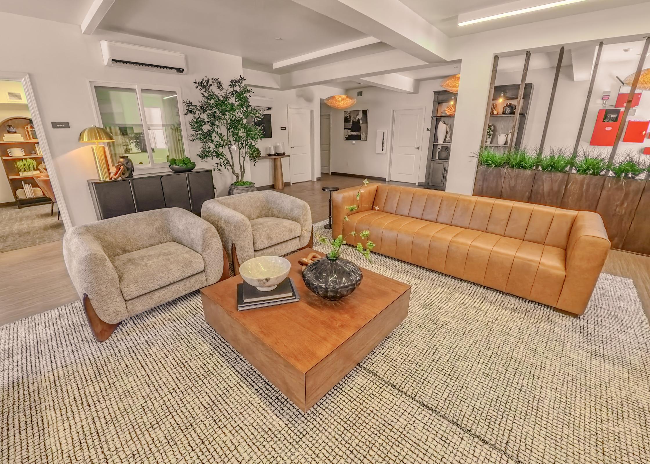 A modern living space with two plush armchairs and a leather sofa, arranged around a wooden coffee table. Decorative plants and stylish light fixtures enhance the ambiance, while a textured rug adds warmth to the room. The walls are neutral, creating a cozy and inviting atmosphere.