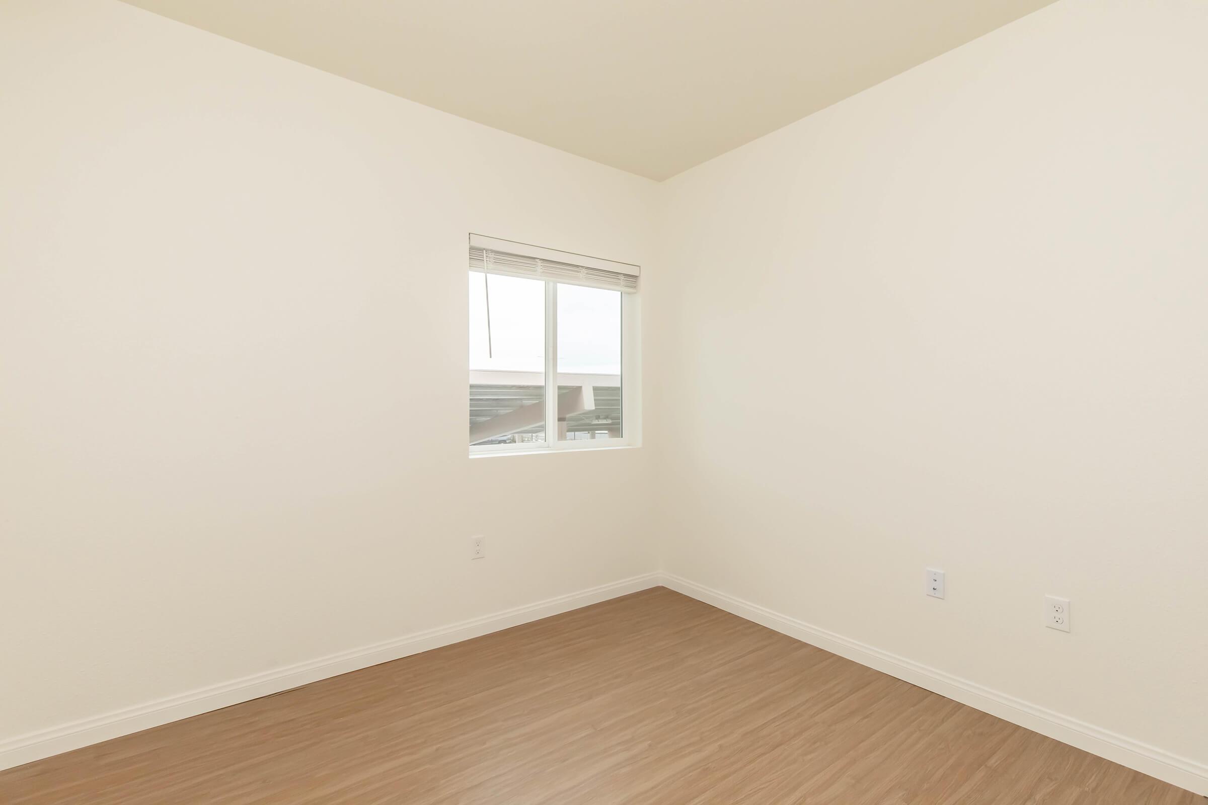 Empty room with light-colored walls and a wooden floor. A single window is visible, allowing natural light to enter. The space appears clean and unfurnished, creating an inviting atmosphere for potential occupants.