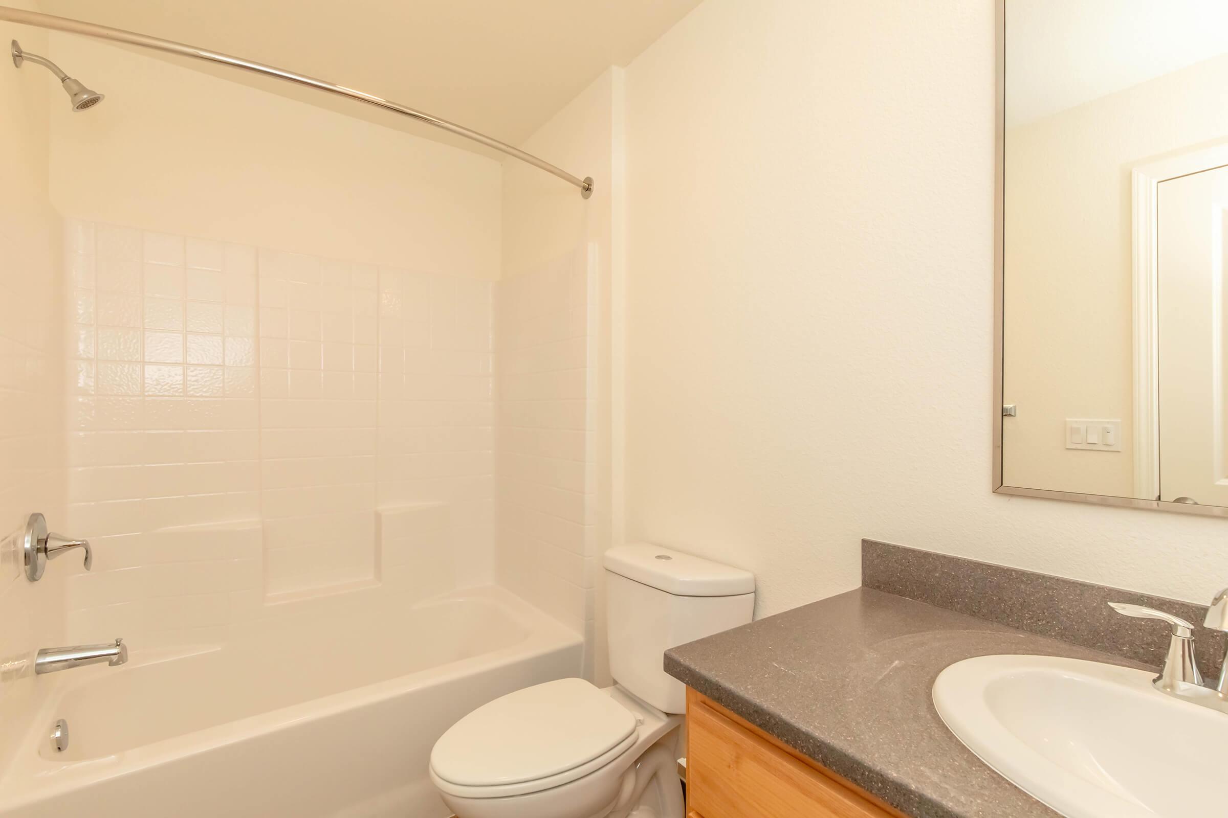 A clean, modern bathroom featuring a white bathtub and shower combination, a toilet, and a countertop sink with a faucet. The walls are painted in light colors, and a mirror is mounted above the sink. The space is bright and uncluttered, creating a fresh and inviting atmosphere.