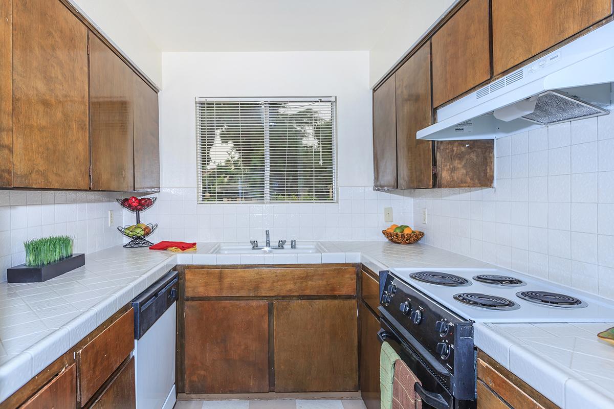 A modern kitchen featuring wooden cabinets, white countertops, a stove, and a sink.