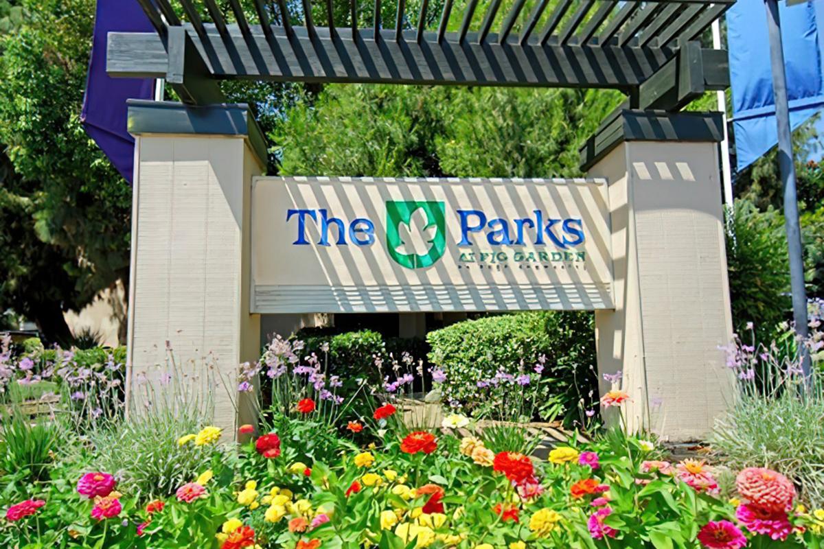 A colorful garden sign reading "The Parks at Fig Garden," surrounded by vibrant flowers and greenery, with a decorative structure above the sign.