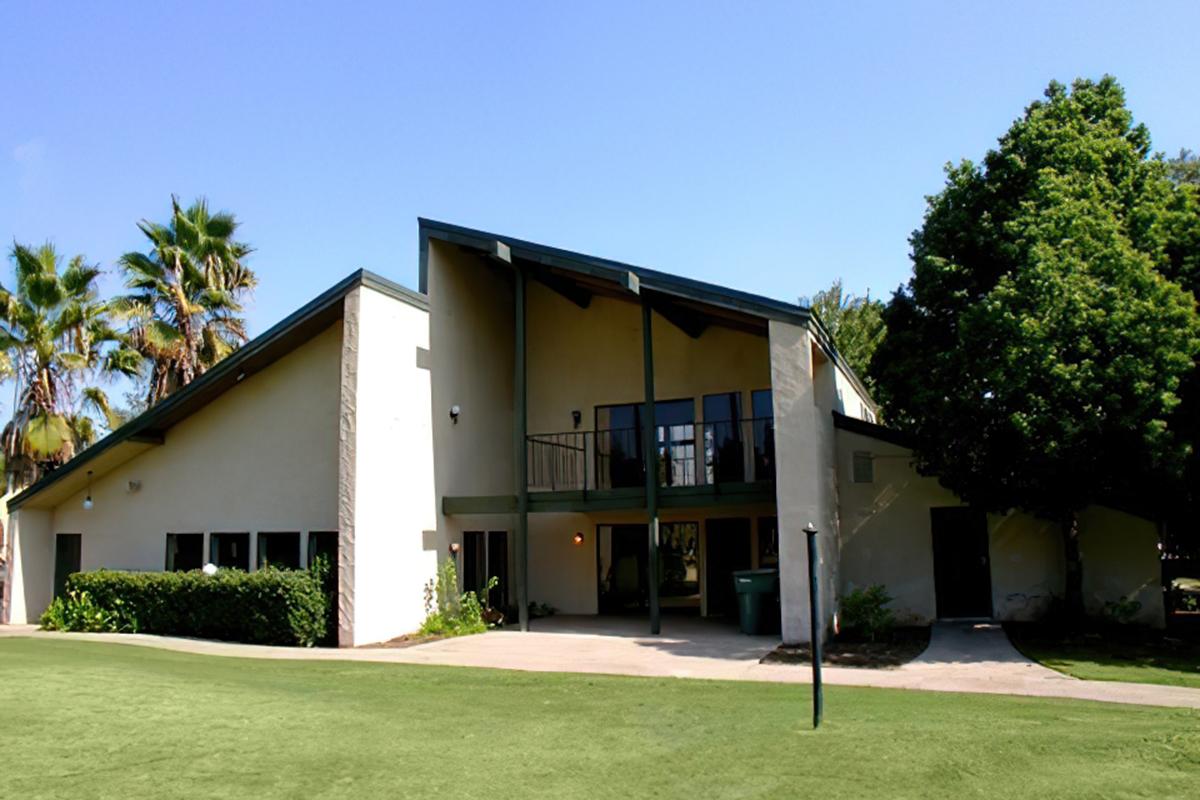A modern-style building with a sloped roof, surrounded by lush greenery and palm trees. 