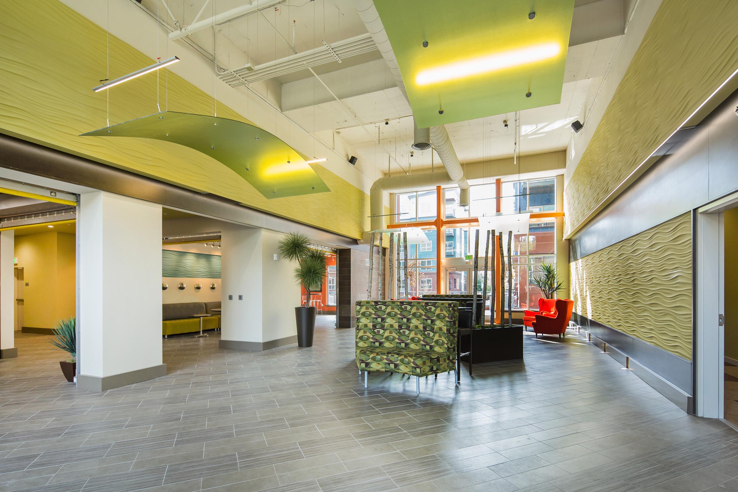 Modern interior of a spacious lobby with high ceilings, featuring green and cream walls, stylish furniture, and contemporary decorations.