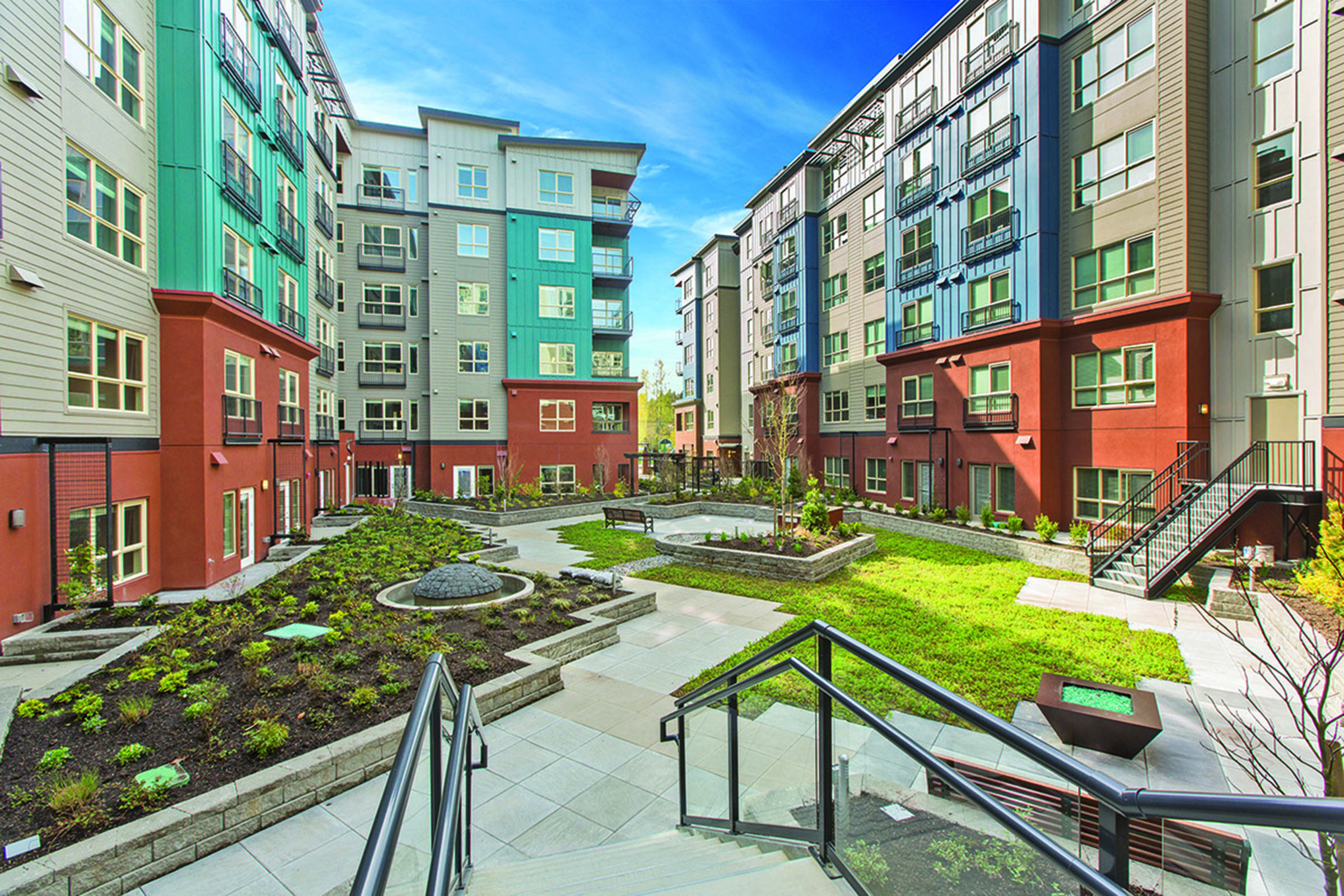 Modern apartment complex courtyard featuring landscaped gardens, stone pathways, and benches.