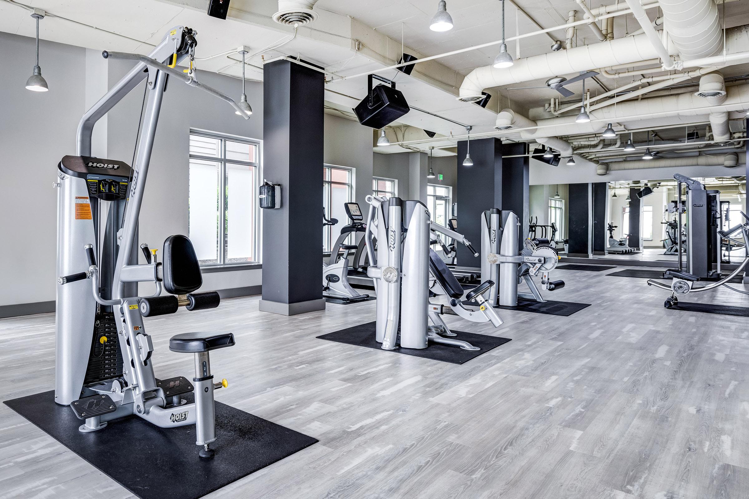 A spacious, modern gym interior featuring various exercise machines, including weight training equipment and cardio machines.