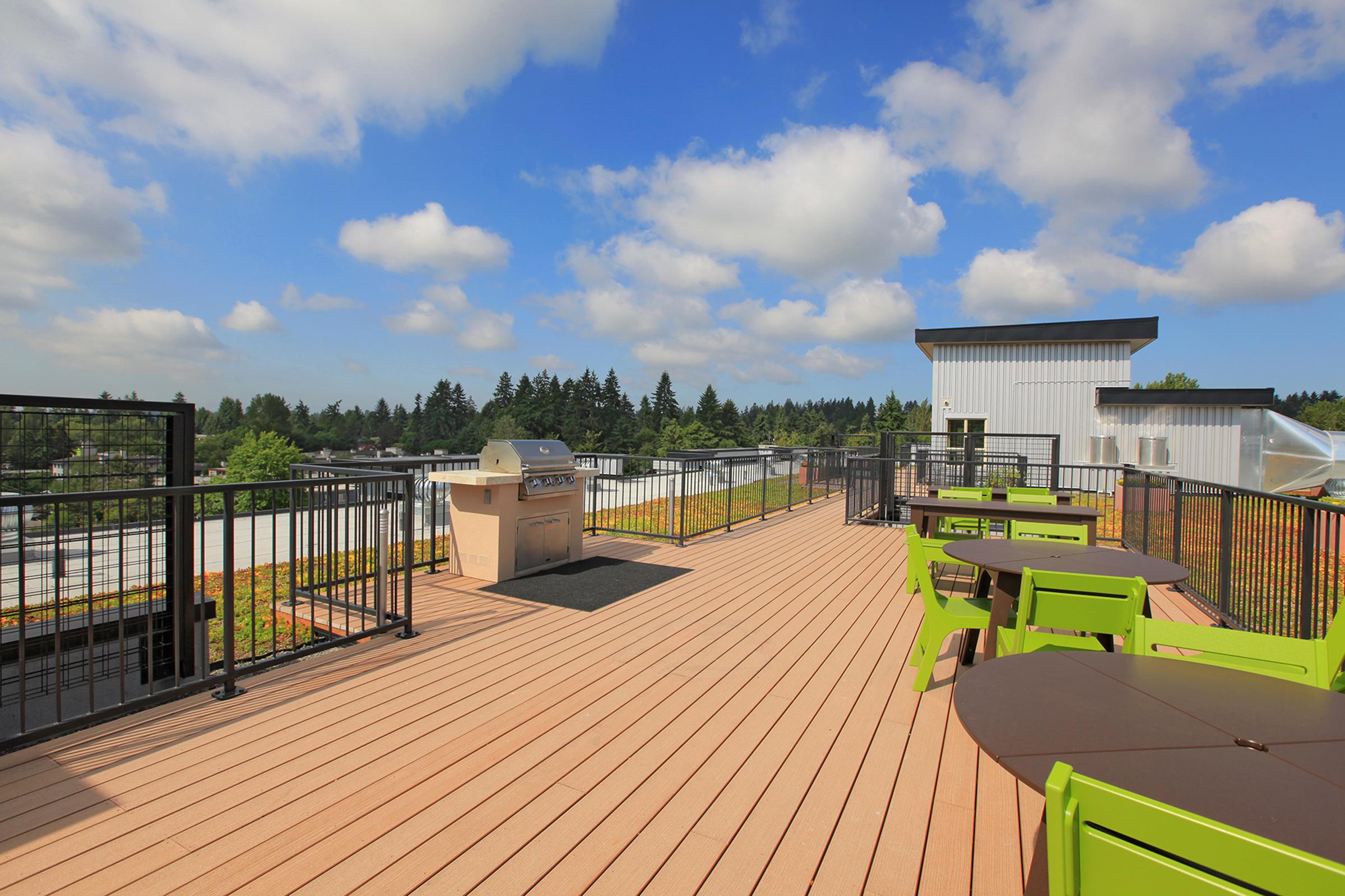 A spacious rooftop terrace with wooden decking, featuring green outdoor furniture and a grill. 