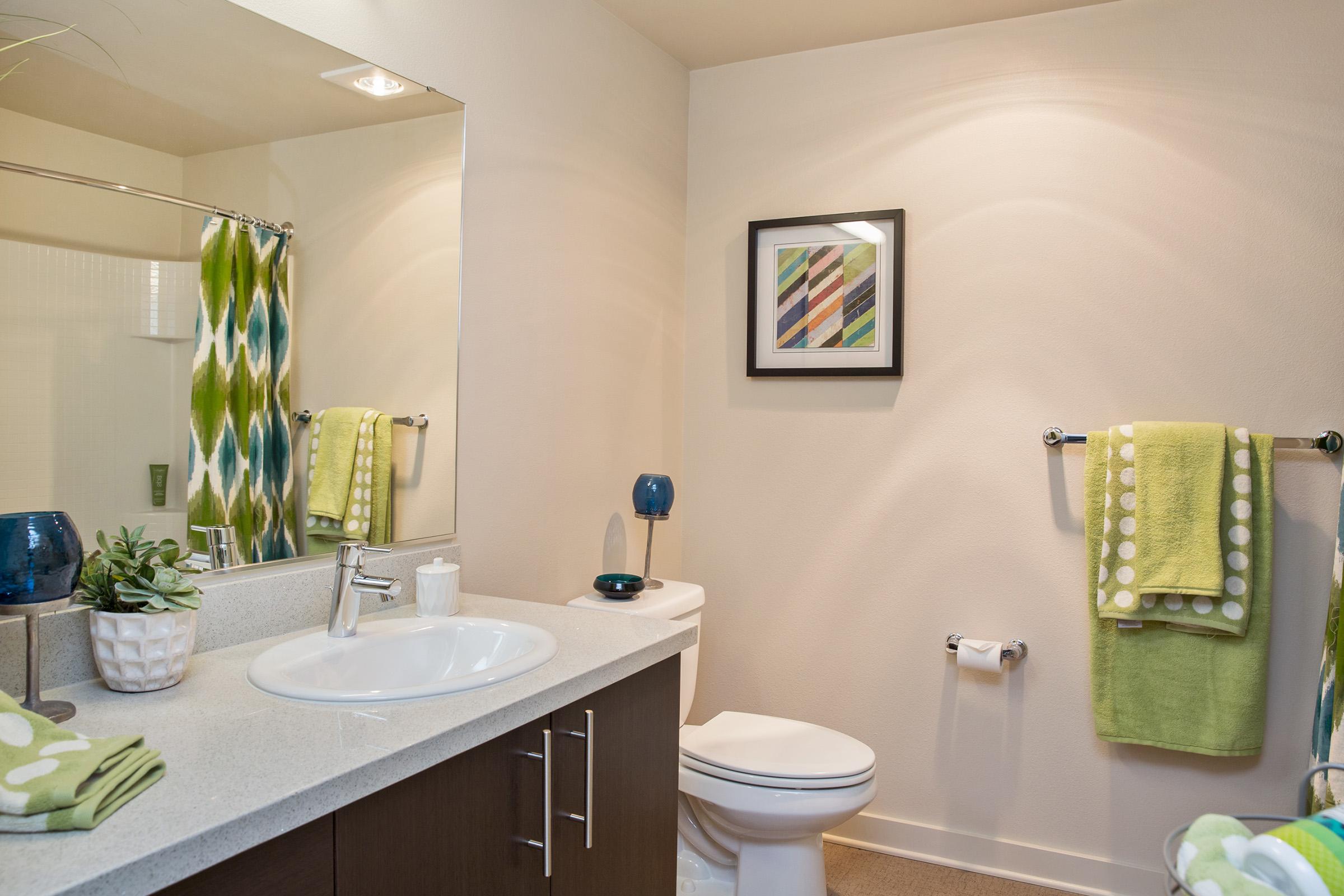 A modern bathroom featuring a white sink with a mirror above, a toilet, and a decorative framed artwork on the wall.