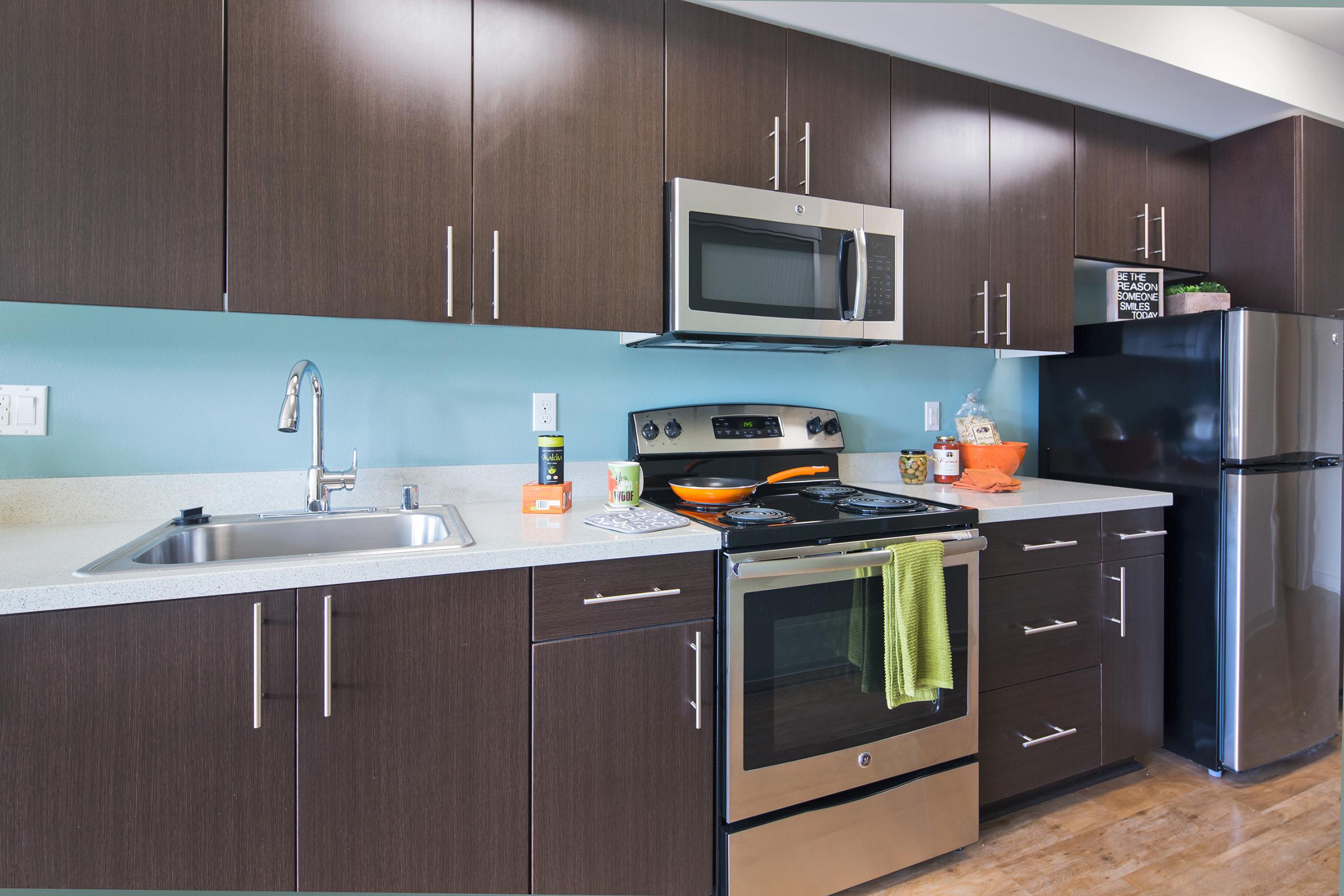 Modern kitchen featuring dark wood cabinetry, stainless steel appliances, a microwave above an oven, and a black refrigerator.