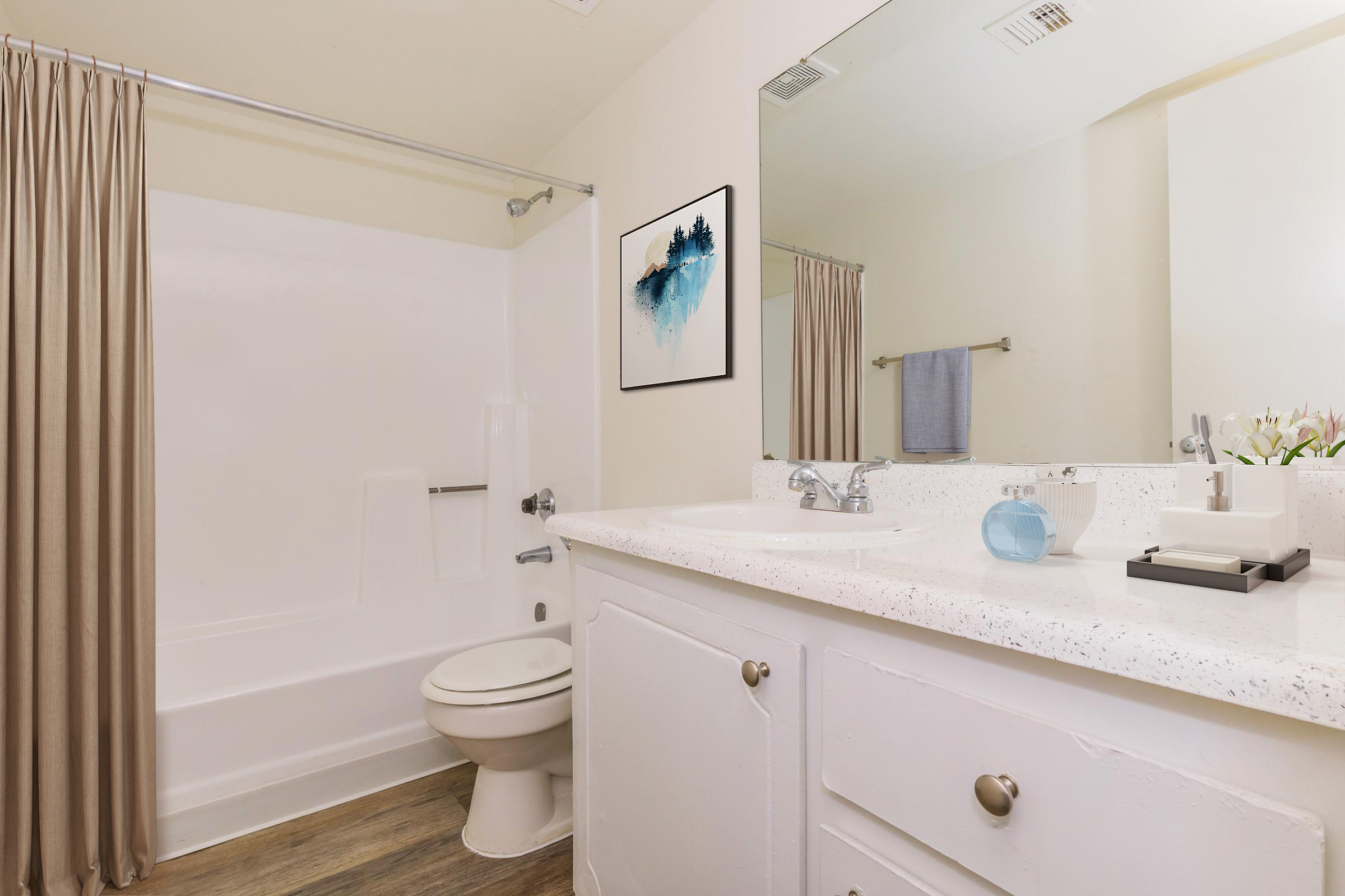 A clean and modern bathroom featuring a white bathtub with a shower curtain, a vanity with a speckled countertop, a mirror above the sink, and a small decorative arrangement on the counter. The walls are painted light, and natural light illuminates the space.