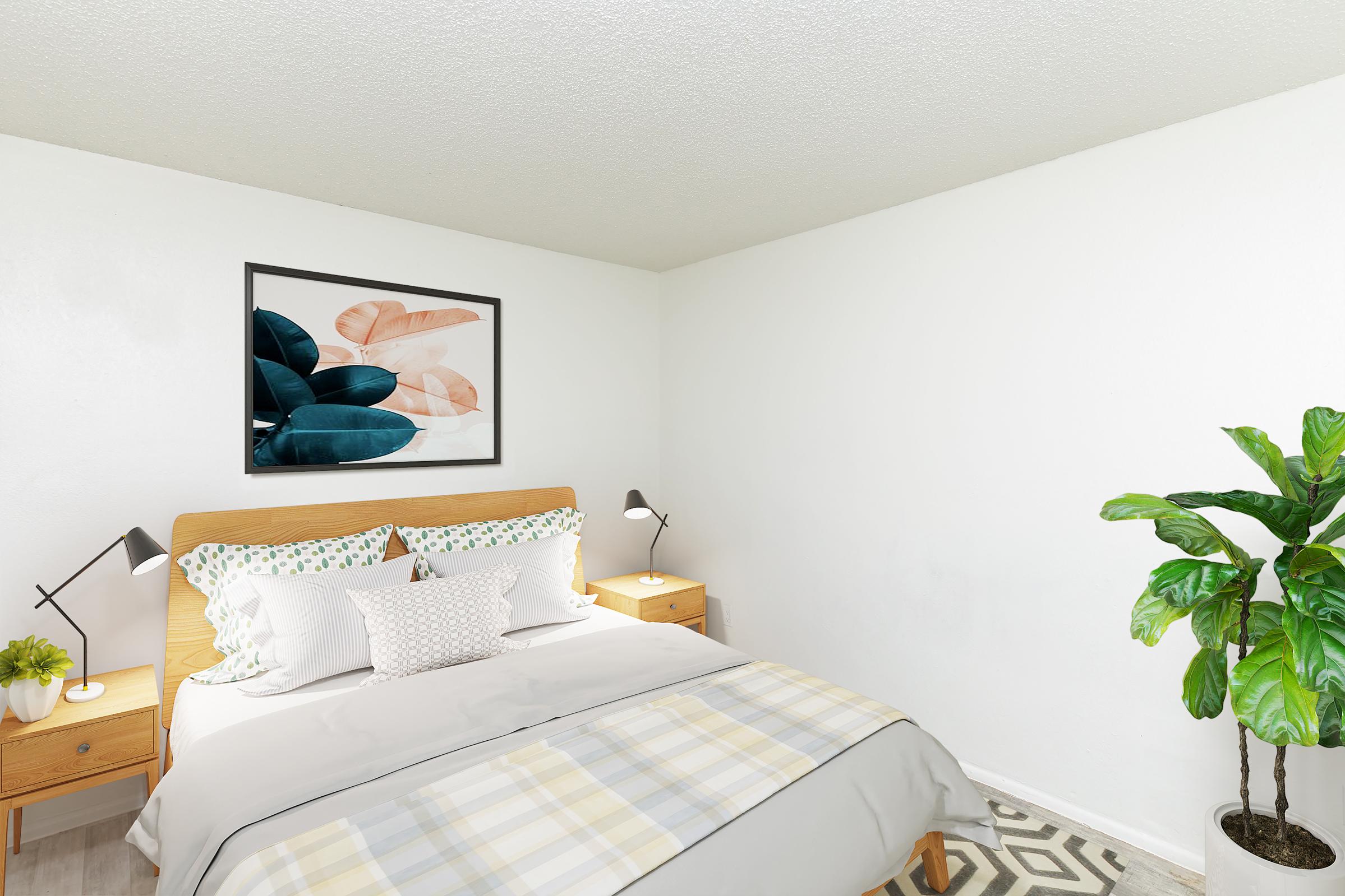 A cozy bedroom featuring a wooden bed frame with a light gray blanket and decorative pillows. On either side of the bed are wooden nightstands with lamps. A framed artwork of leaves hangs on the wall, and a potted plant adds greenery to the space. The room has a bright, welcoming atmosphere.
