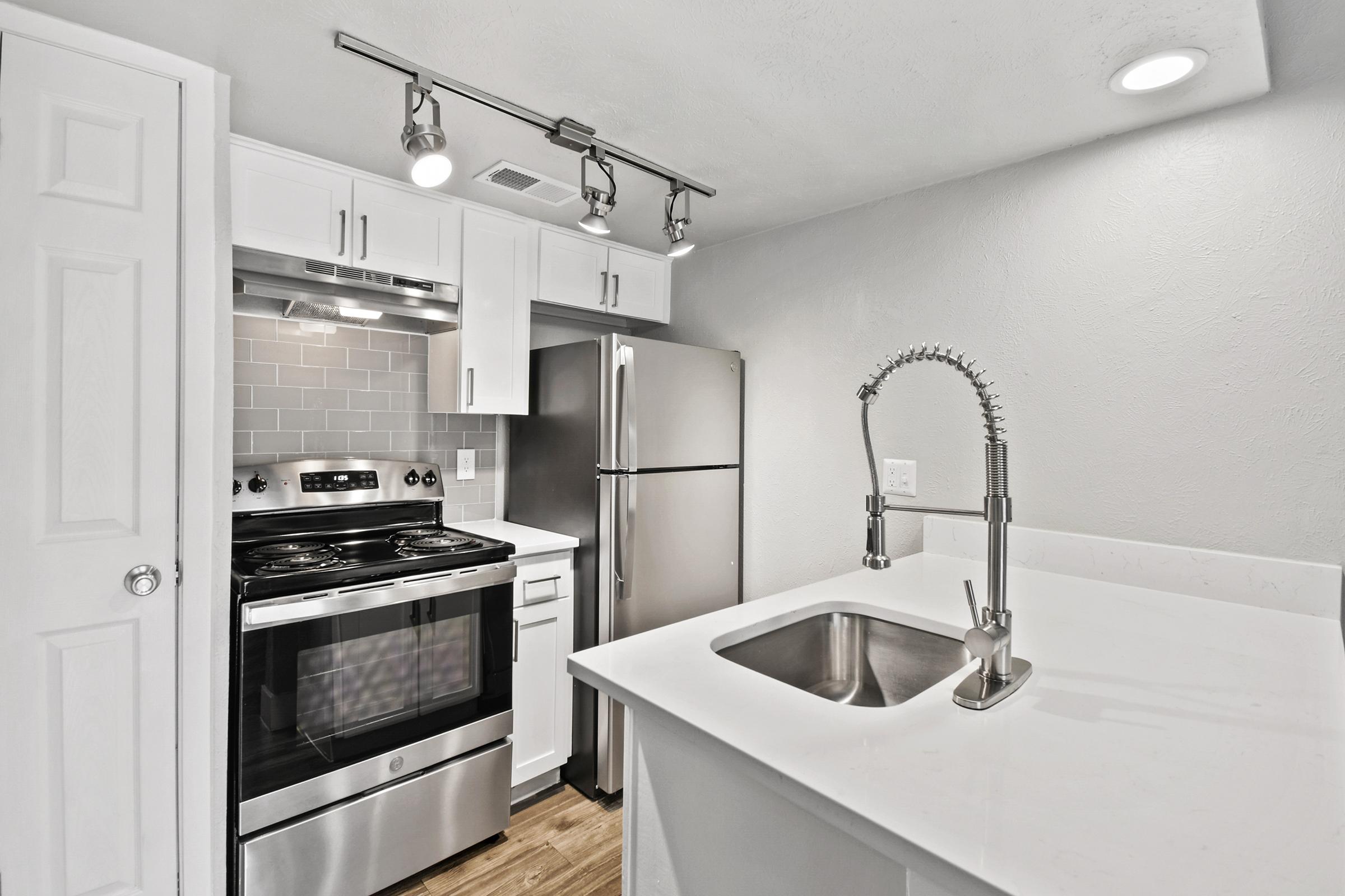 Modern kitchen featuring stainless steel appliances, including an oven and refrigerator, sleek white cabinetry, and a quartz countertop with a sink. The room is well-lit with recessed lighting and has a clean, contemporary design.