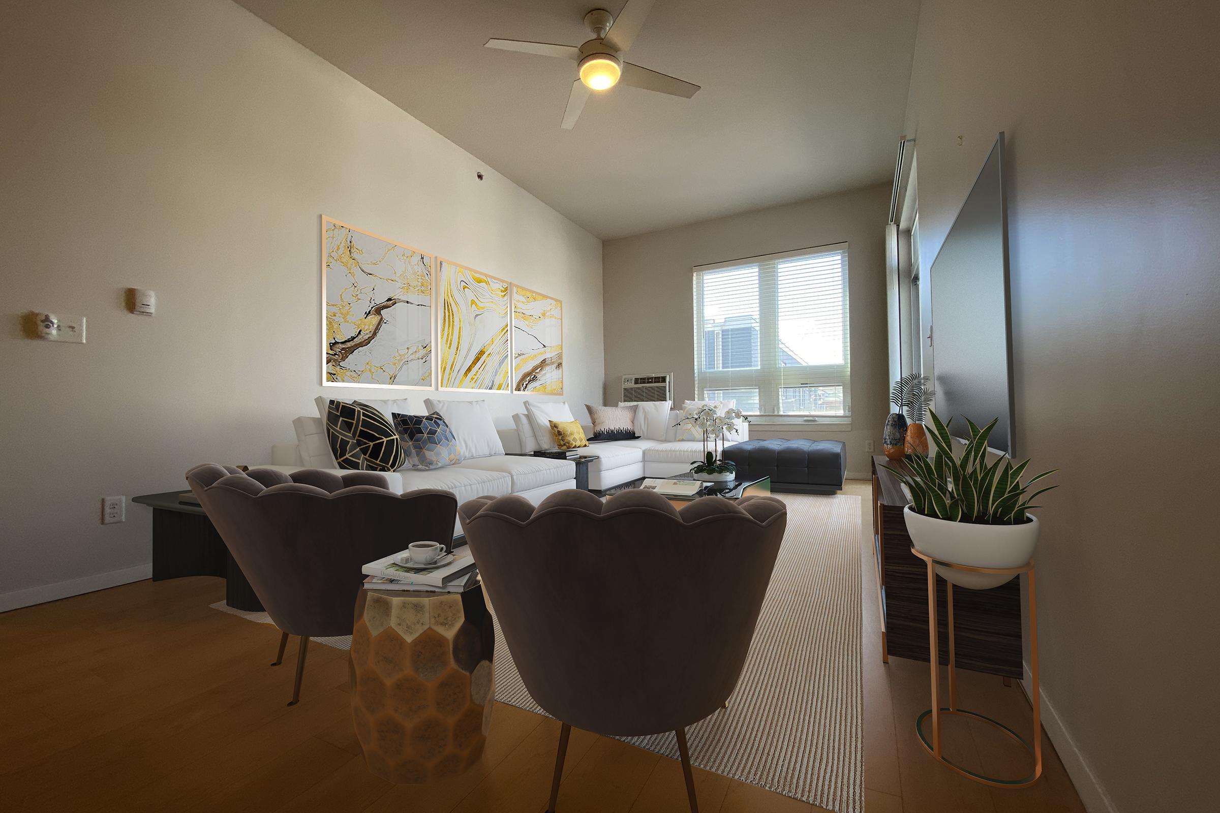 A stylish living room featuring a light-colored sectional sofa with decorative pillows, a large abstract art piece on the wall, a sleek coffee table, and two elegant armchairs. Natural light streams in from a window, highlighting the wooden flooring and potted plants that add a touch of greenery to the space.