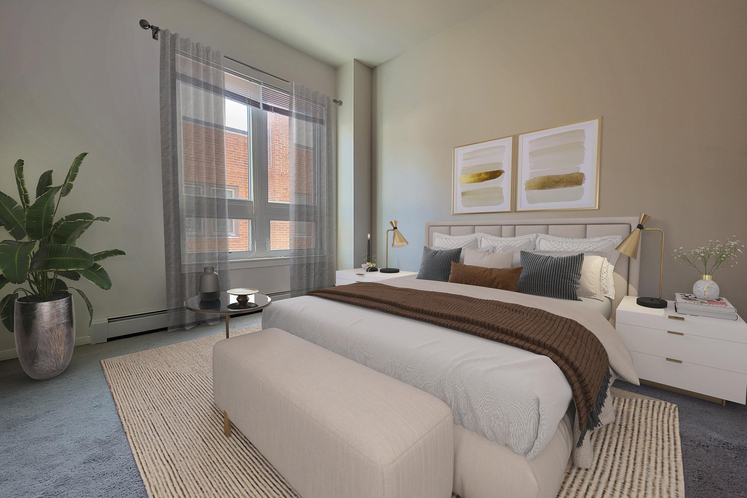 A cozy bedroom featuring a large bed with decorative pillows and a throw blanket, a bedside table with a lamp, and a stylish bench at the foot of the bed. Natural light streams in from large windows, highlighting a plant in a pot and a minimalistic coffee table with decorative items.