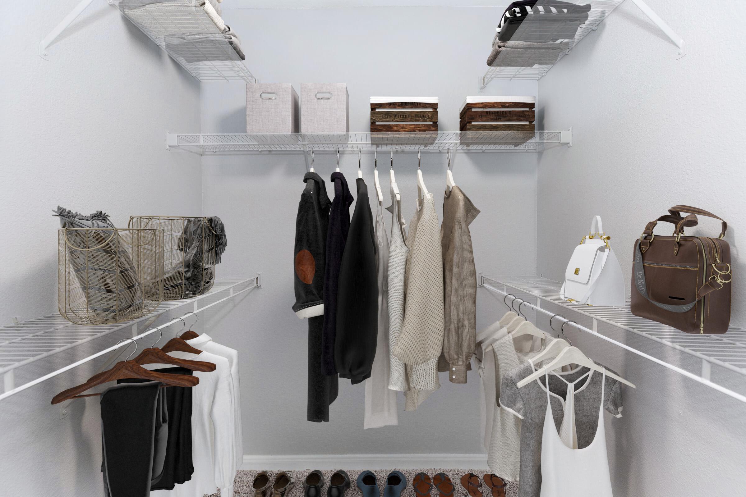 A well-organized closet featuring hanging clothes, including shirts and jackets, along with various storage boxes and baskets. The floor displays a selection of shoes, and there are also handbags on a shelf. The closet has a light gray wall and wire shelving for easy visibility and access.