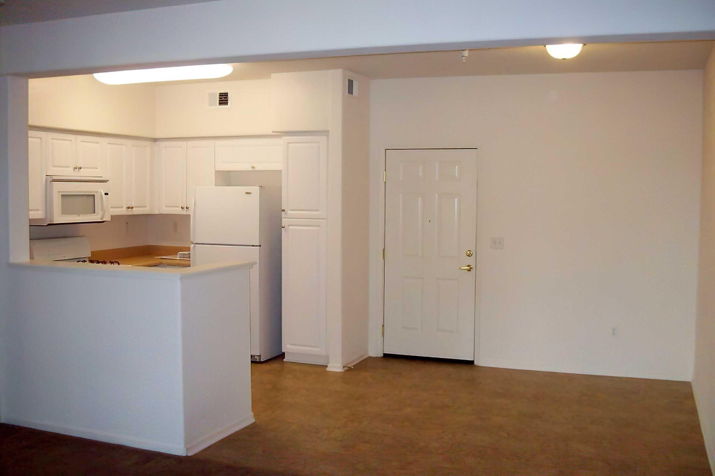 View of a small, empty apartment interior featuring a kitchen with white cabinets, a microwave, and a refrigerator