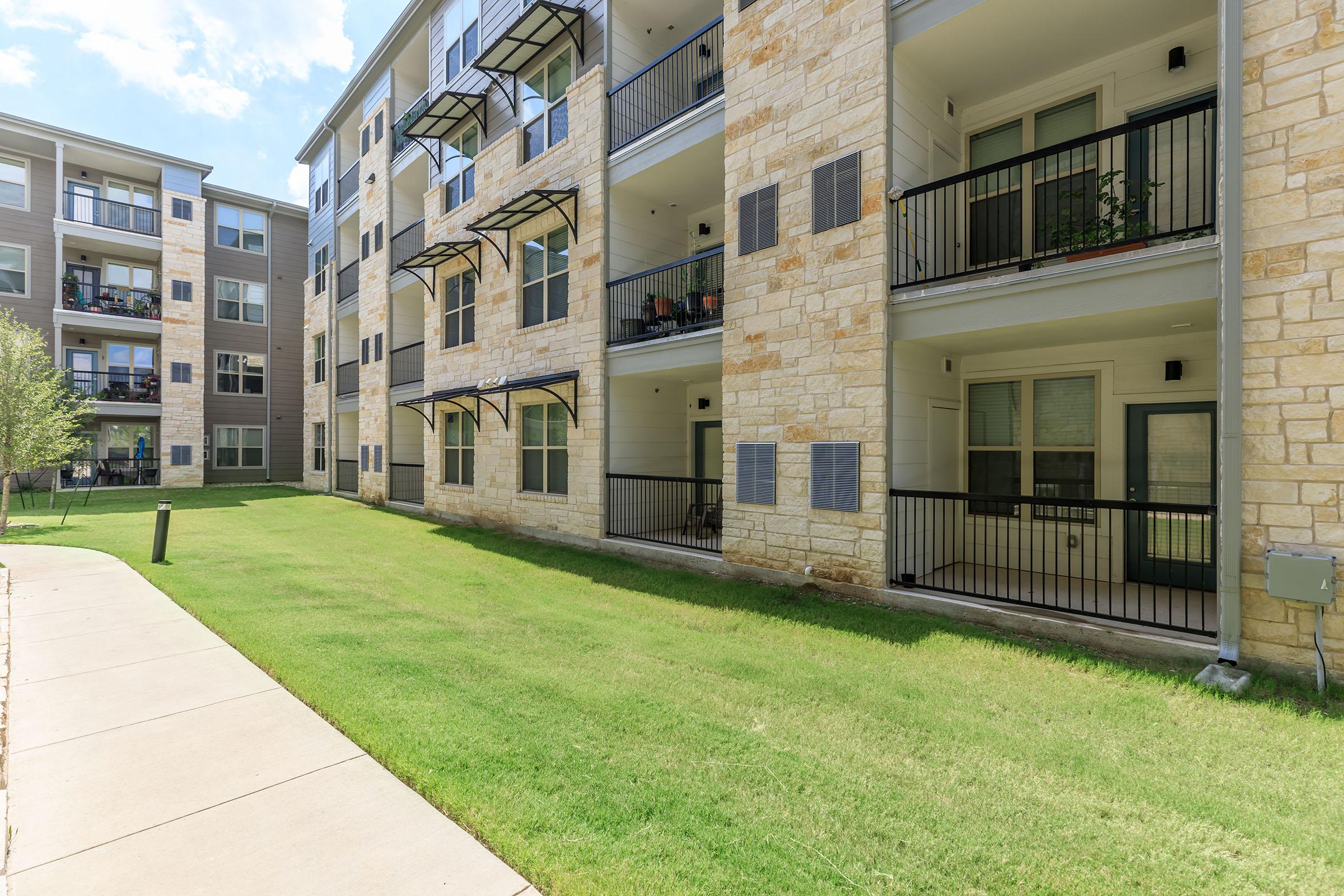 Pflugerville Senior Living - Legacy Ranch at Dessau East - Exterior View Of Lush Green Lawn In Front Of Three-Story Building Featuring White Stone Walls and Private Patio Balconies