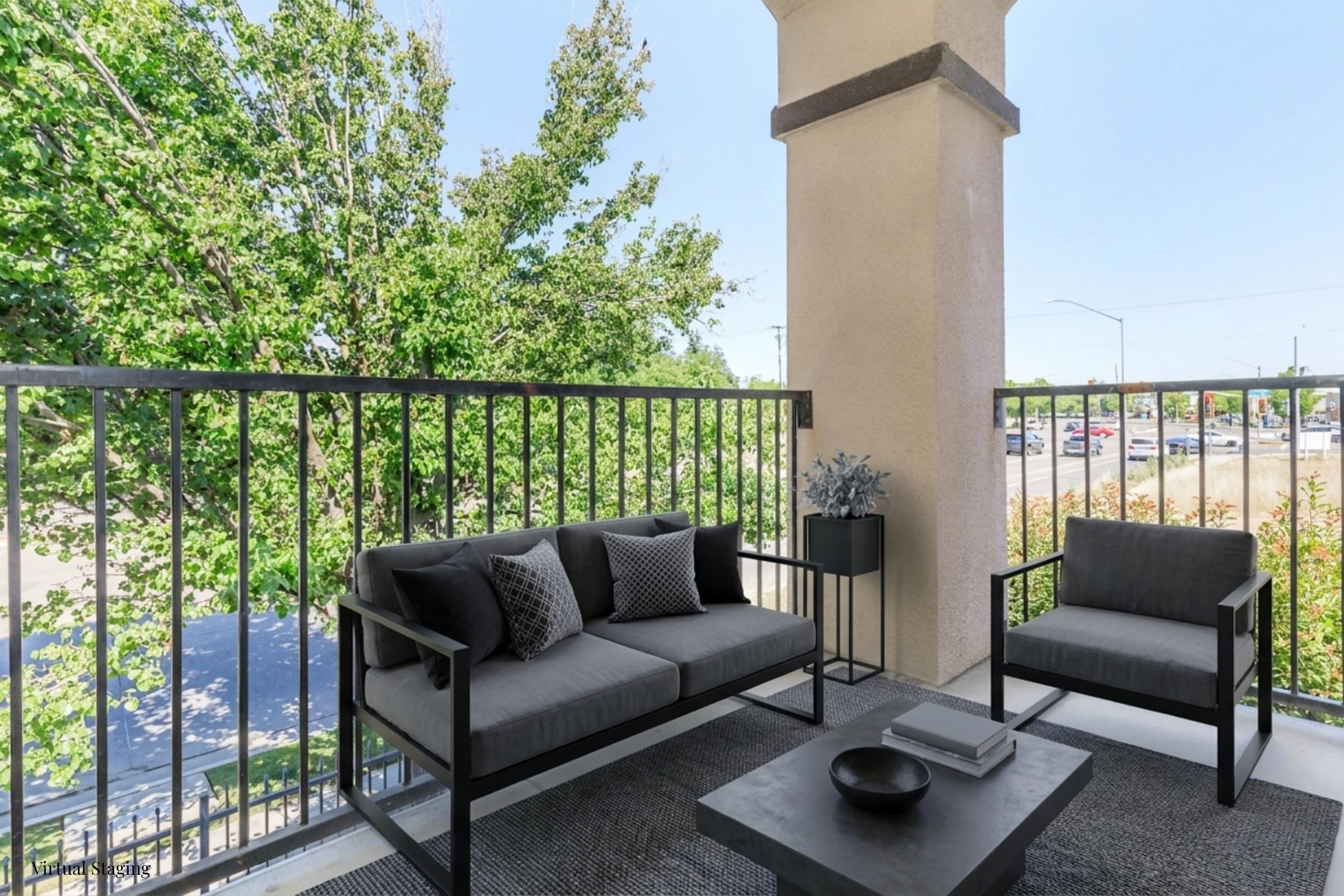 A cozy balcony with modern outdoor furniture featuring a sofa and coffee table, surrounded by greenery. The space is designed for relaxation, showcasing a potted plant on the table and a lovely view of the trees and street below.