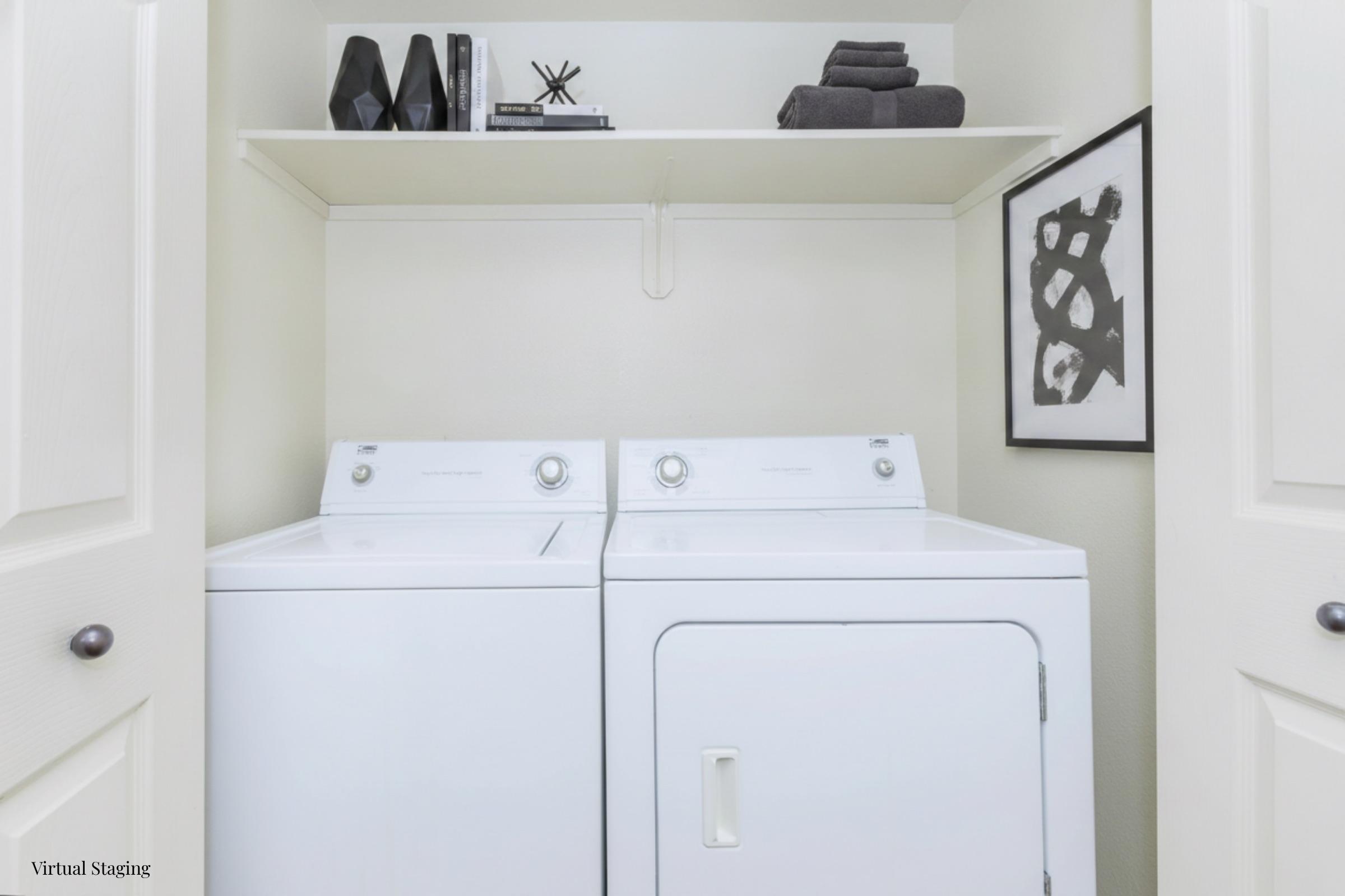 A modern laundry room featuring a white washing machine and dryer side by side. Above, there is a shelf with black decorative items and neatly folded dark towels. A framed abstract black and white art piece hangs on the wall, complementing the clean and organized space.
