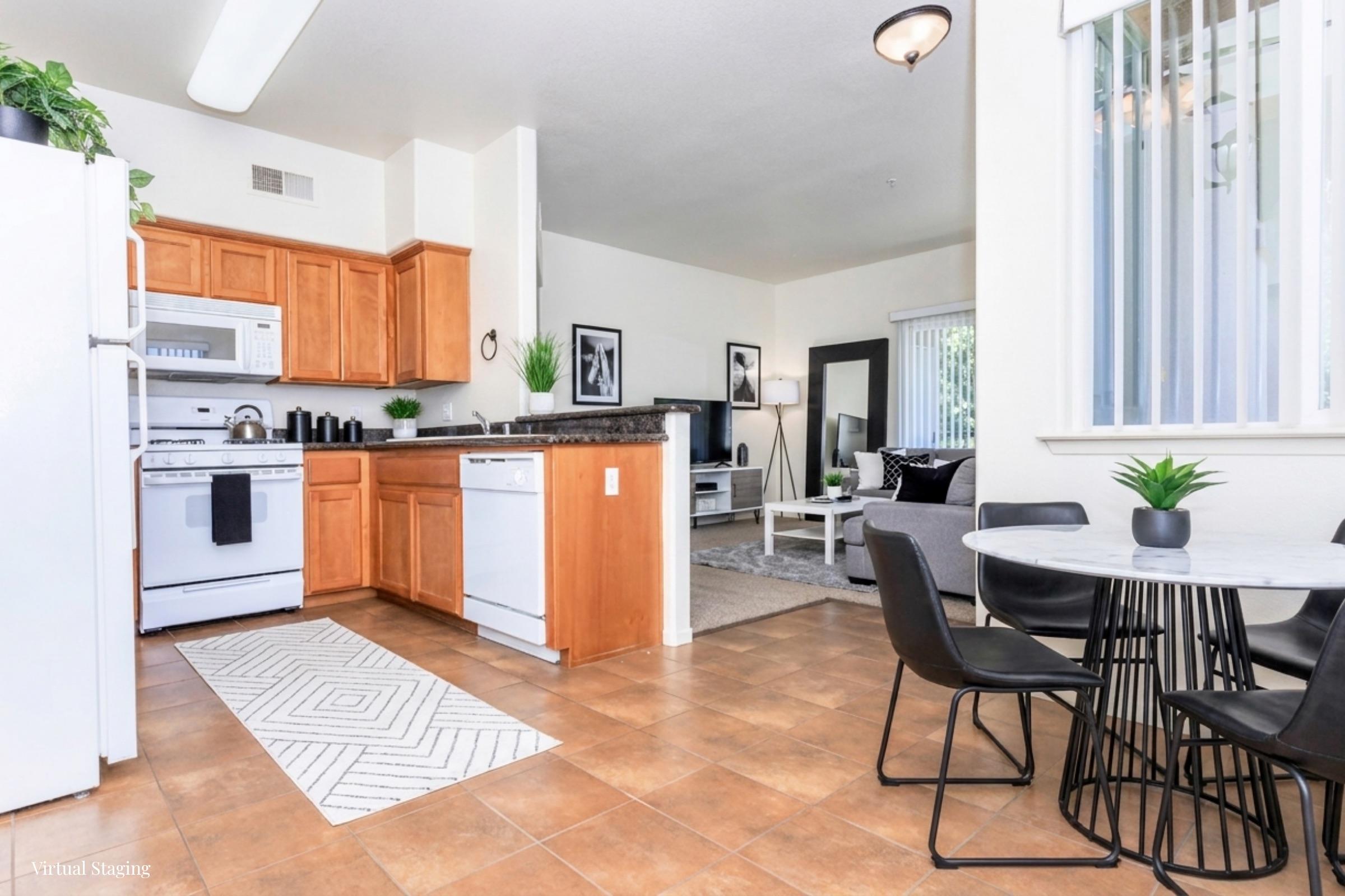Modern kitchen and dining area featuring wooden cabinets, a white refrigerator, and a black and white color scheme. The space includes a dining table with black chairs, a cozy living area with a couch and decorative plants, and large windows allowing natural light.