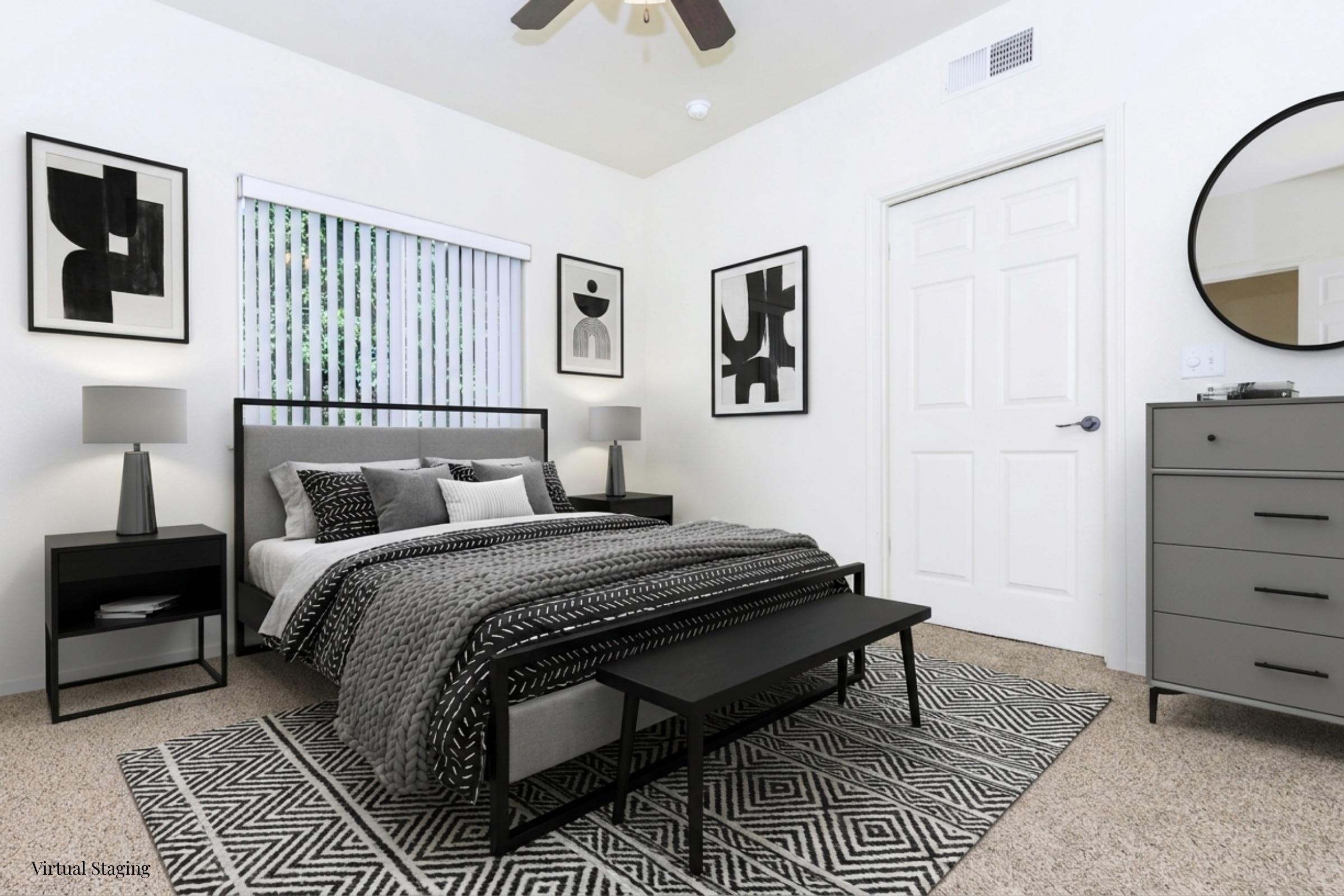 A modern bedroom featuring a bed with a black and white patterned comforter, flanked by two nightstands with lamps. The room has geometric art on the walls, a round mirror, a gray dresser, and a patterned rug. Natural light filters in through a window with blinds.