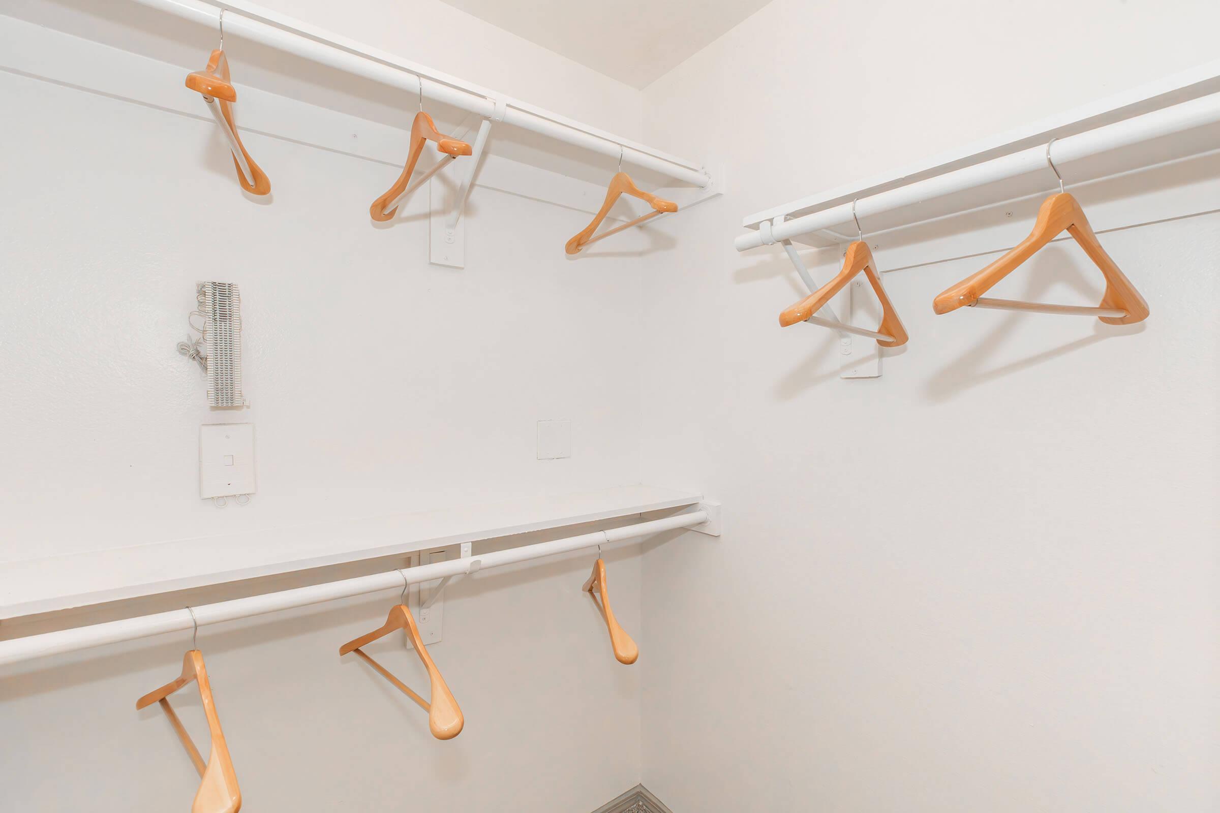 Empty closet with white walls and two hanging rods. Several wooden hangers are suspended from the rods, while a small shelf runs along the back wall. The space is bright and minimalistic, conveying a sense of organization and simplicity.