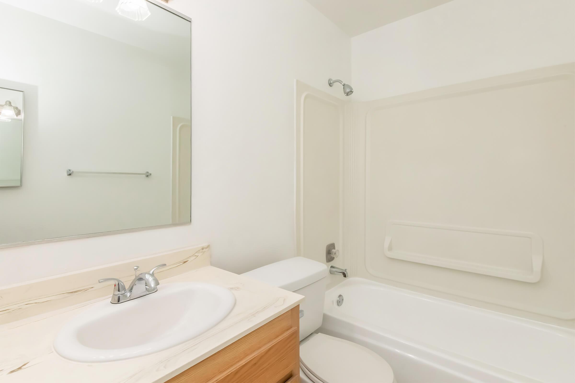 A clean and modern bathroom featuring a white bathtub, shower combination, a sink with a light-colored countertop, and a large mirror above the sink. The walls are painted a light color, and there is a towel rack installed. Natural light fills the space, creating a bright and airy atmosphere.
