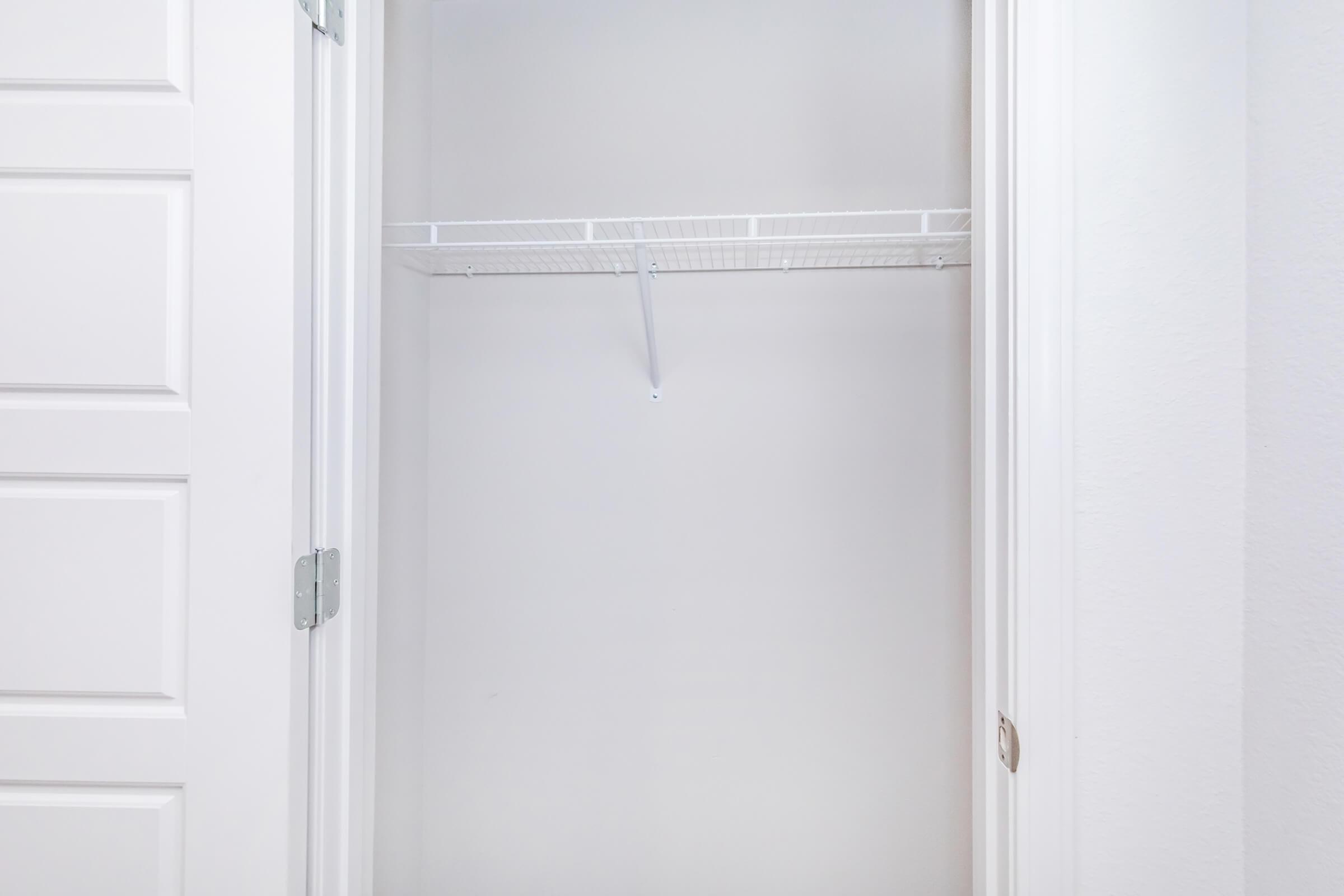 Empty closet with white walls, featuring a wire shelving unit and a hanging rod, visible from an open double door. The space is well-lit and unobstructed, conveying a minimalist and organized appearance.