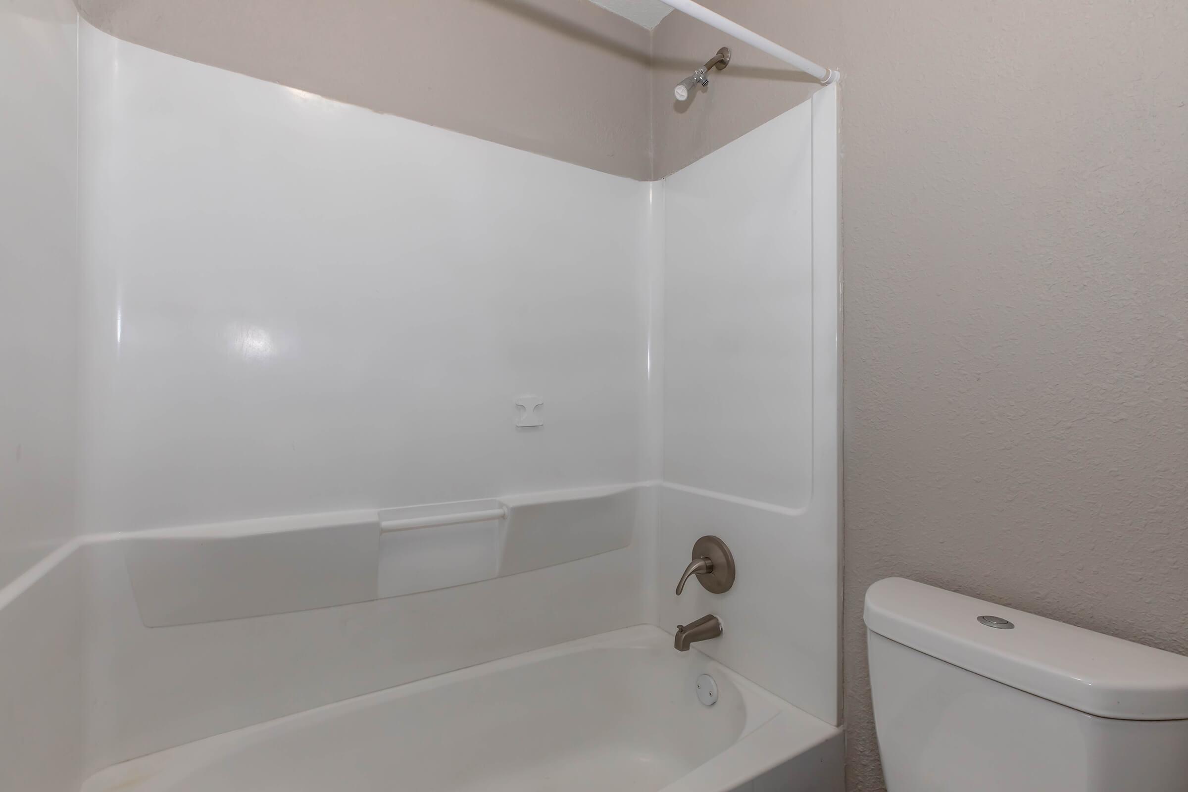 A clean, modern bathroom featuring a white bathtub with a shower head and a toilet. The walls are painted light, and the overall space appears spacious and well-maintained.