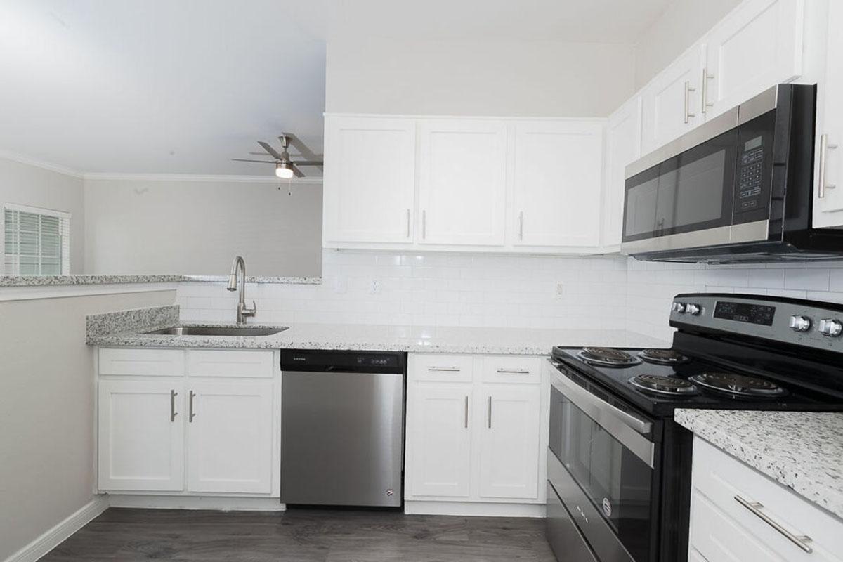 Modern kitchen featuring white cabinets, granite countertops, stainless steel appliances including a refrigerator, microwave, and dishwasher. The space is well-lit with natural light, and includes a sleek design with an open layout, ideal for cooking and entertaining.