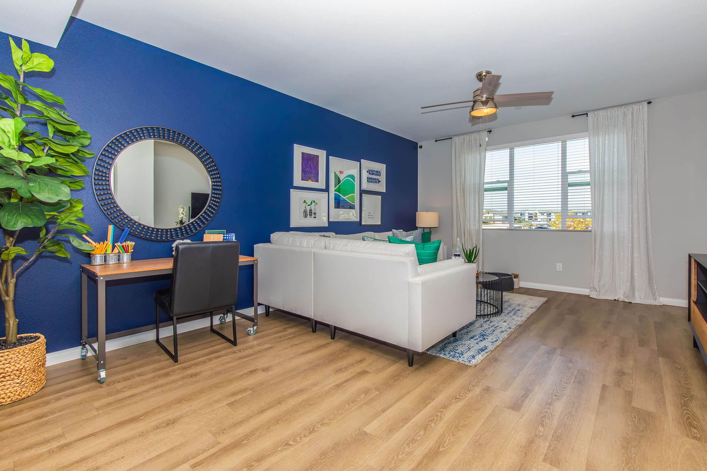 Apartments Near Vandenberg Air Force Base in Santa Maria, CA - Azure Apartments - Living Room with a Sectional Couch, a Ceiling Fan, and a Desk to Work at.