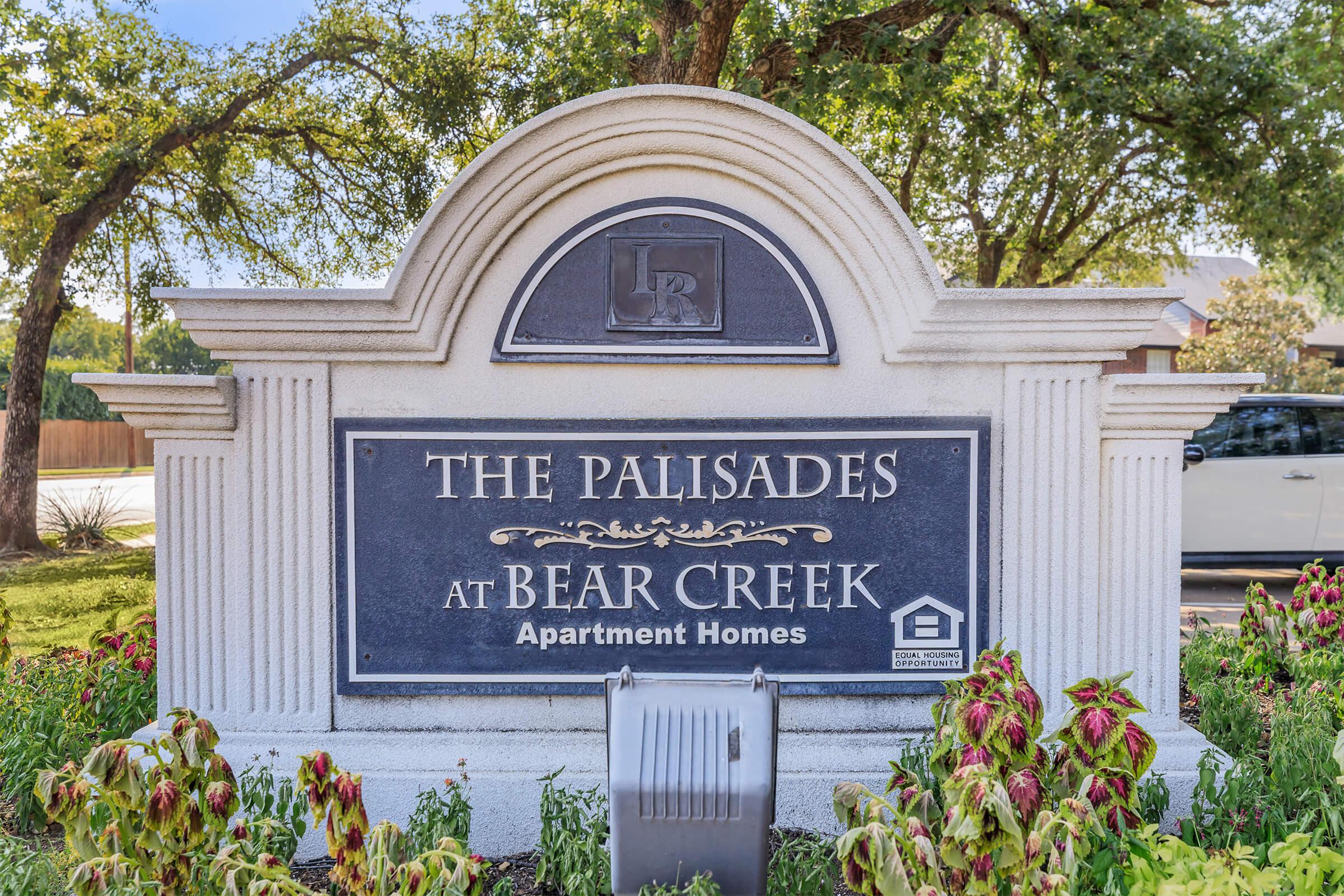 Sign for "The Palisades at Bear Creek Apartment Homes" featuring decorative elements and landscaping around the base.