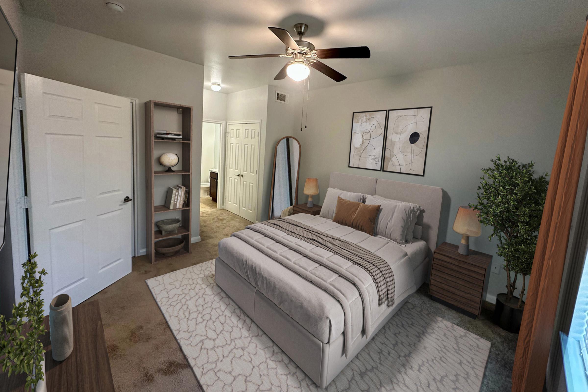 A cozy bedroom featuring a neatly made bed with gray bedding, two decorative pillows, and a modern headboard. The room includes a brown nightstand with a lamp, a bookshelf with decor items, and framed wall art. Natural light combines with soft lighting from a ceiling fan, creating a warm and inviting atmosphere.