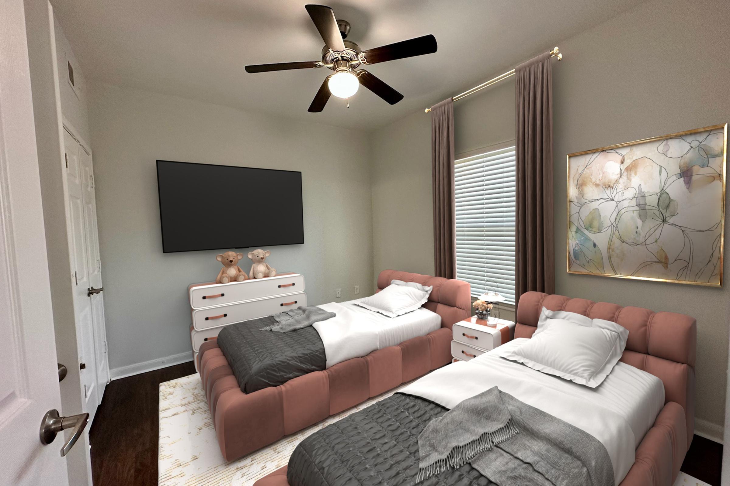 A cozy bedroom featuring two twin beds with pink upholstered frames, gray bedding, and decorative pillows. There is a large flat-screen TV mounted on the wall, a window with light curtains, and a piece of abstract art hanging nearby. The room has a warm atmosphere with a ceiling fan and wooden flooring.