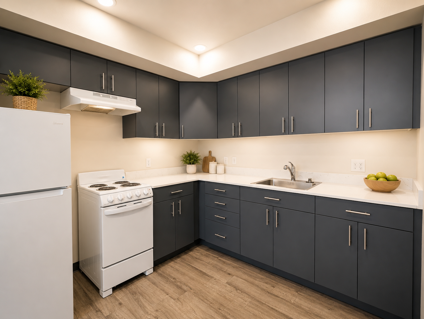 Modern kitchen featuring dark blue cabinets, white countertop, white stove, and refrigerator. A single basin sink is positioned under a wall-mounted cabinet. Greenery in pots adds a touch of nature, while a wooden bowl with green apples sits on the countertop. Warm lighting enhances the inviting atmosphere.