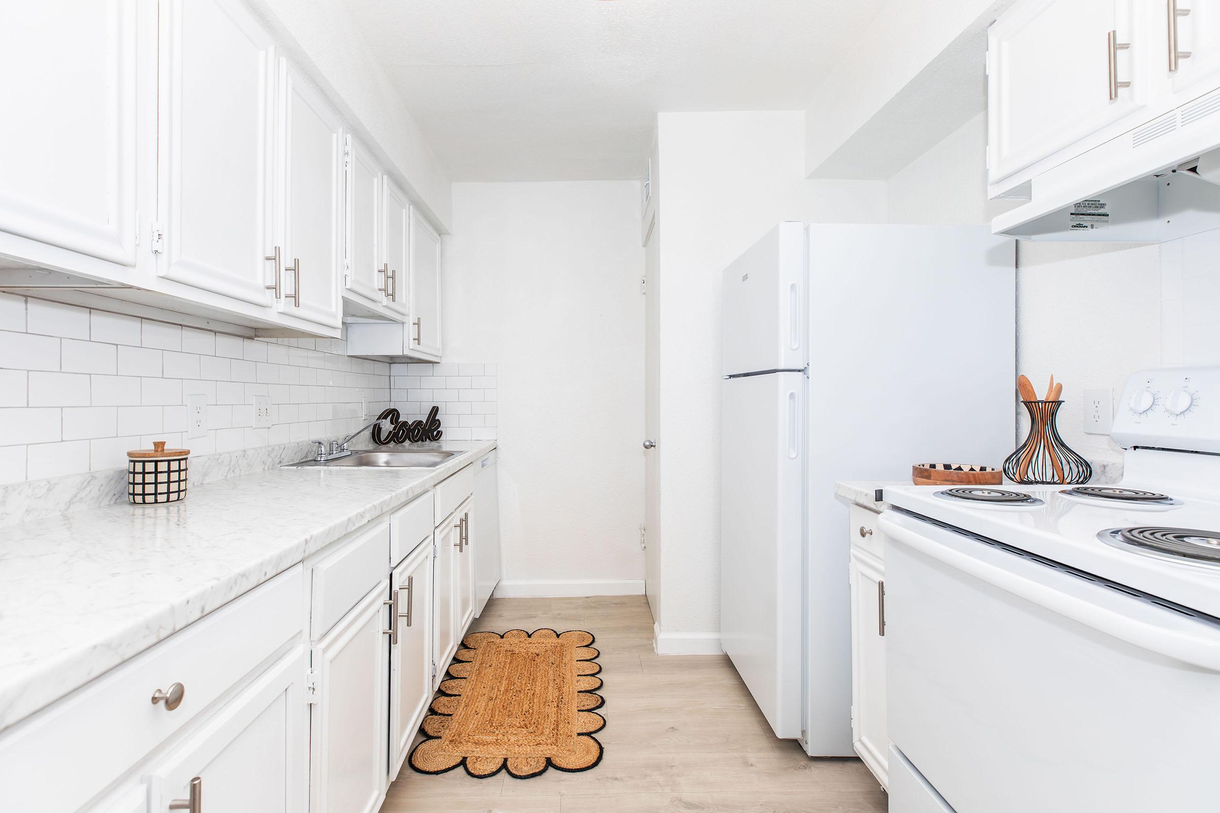 Modern kitchen featuring white cabinetry, a marble countertop, and stainless steel appliances. A light-colored rug adds warmth to the space, and there's a decorative bowl on the counter. The walls are painted in a bright tone, creating an open and inviting atmosphere.
